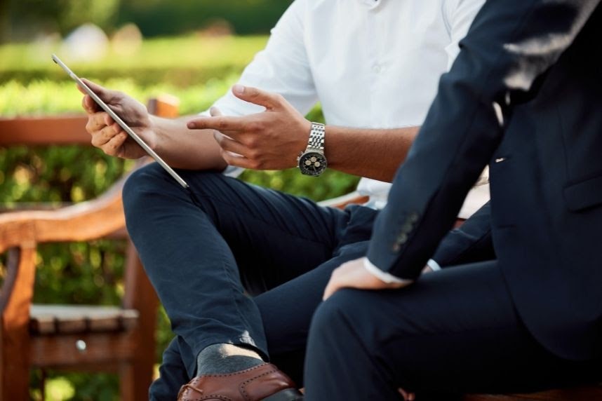 Some people using electronic devices outdoors on a bench.