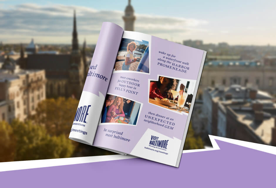An open magazine displays a Visit Baltimore advertisement, showcasing the city's charm and effective brand strategy, set against a blurred cityscape with buildings and a church spire.