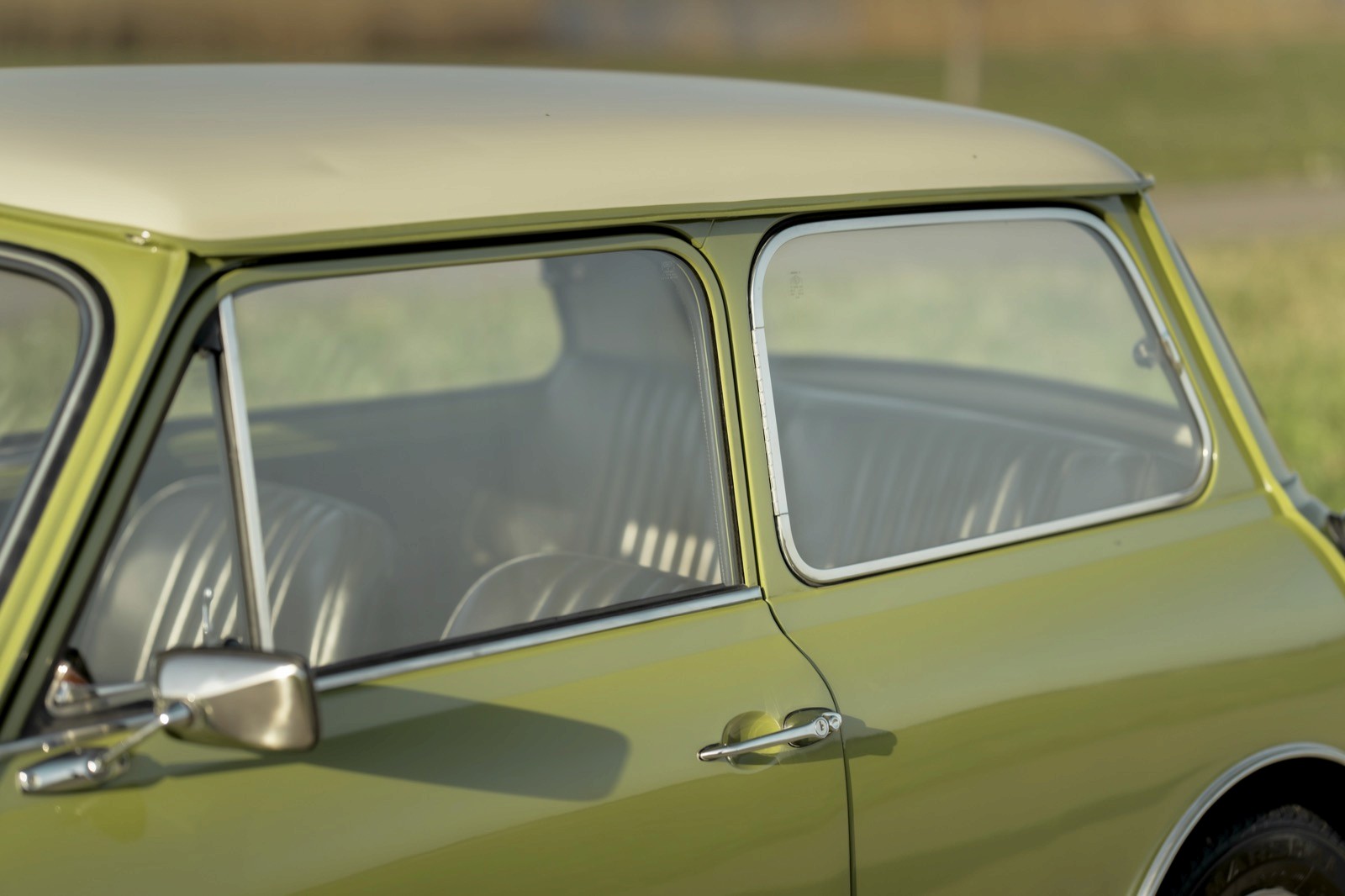 Close-up of a green vintage car's side window, capturing its classic design and chrome accents.