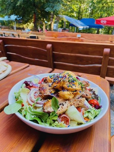 A smiling young man with crossed arms, wearing a plaid shirt and white t-shirt, poses against a dark background.