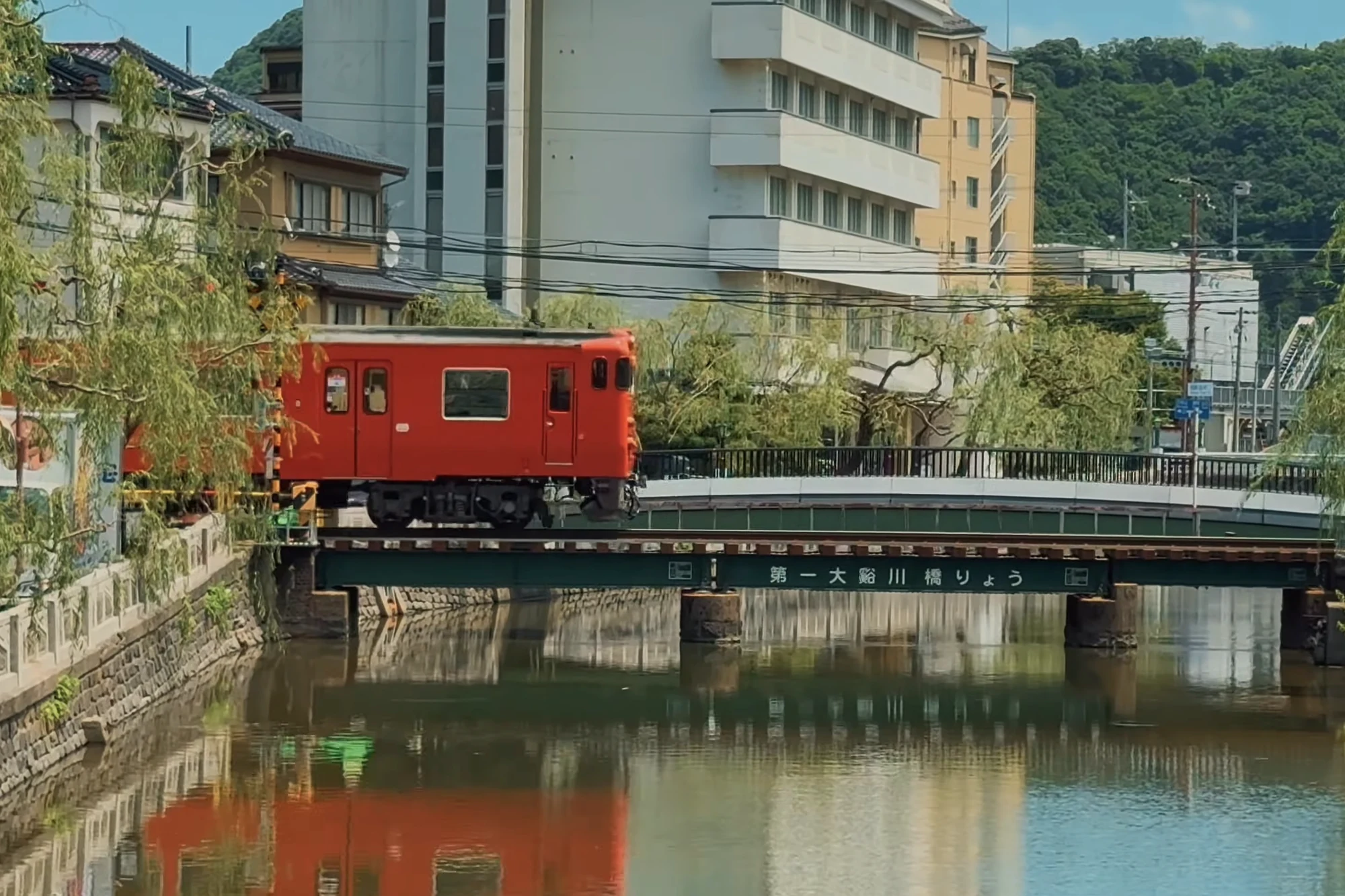 A single red railcar crossing the girder bridge over the Otani river beside Kinosaki.