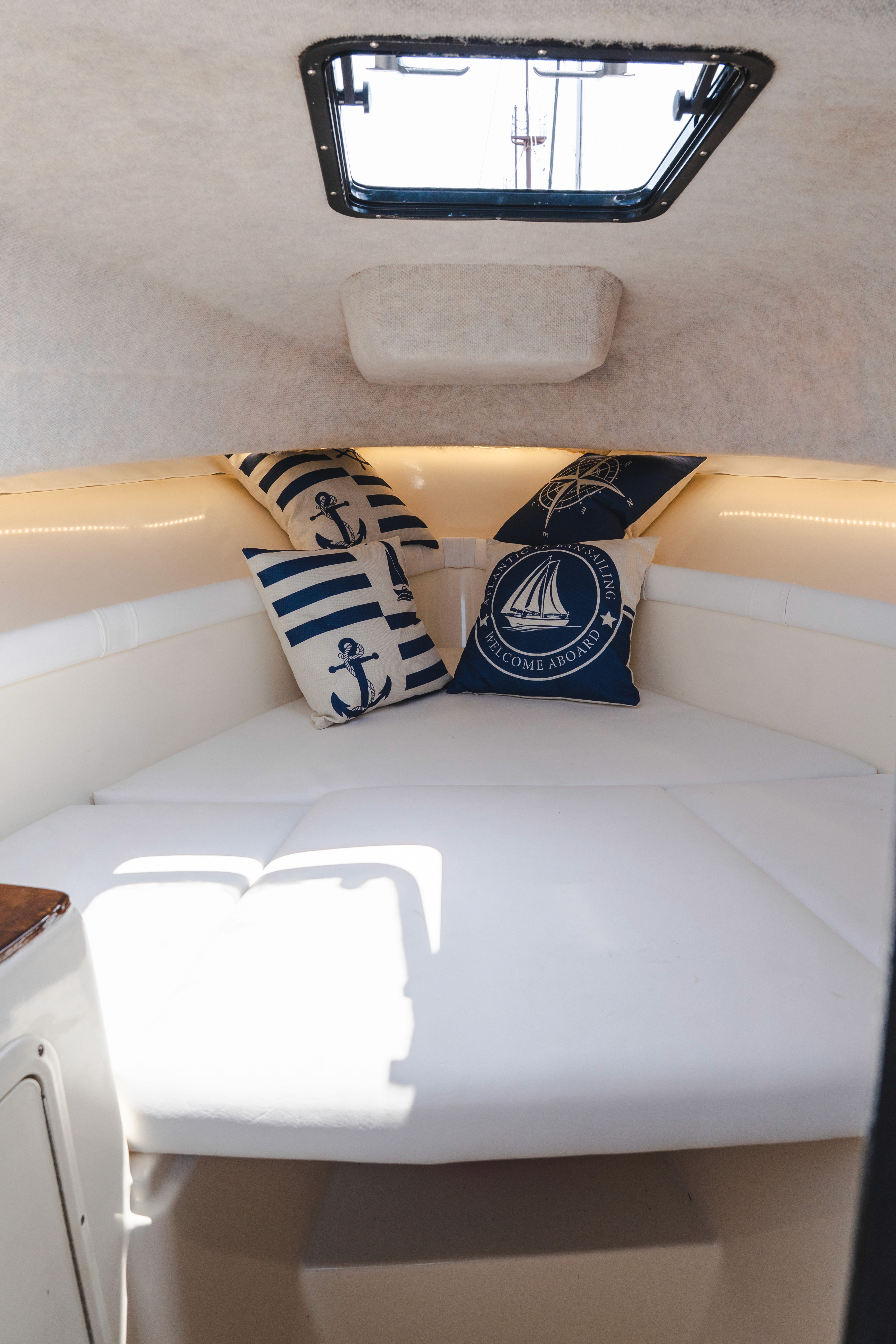 Cozy boat cabin interior with white cushioned seating and nautical decorative pillows featuring anchor and sailboat designs.