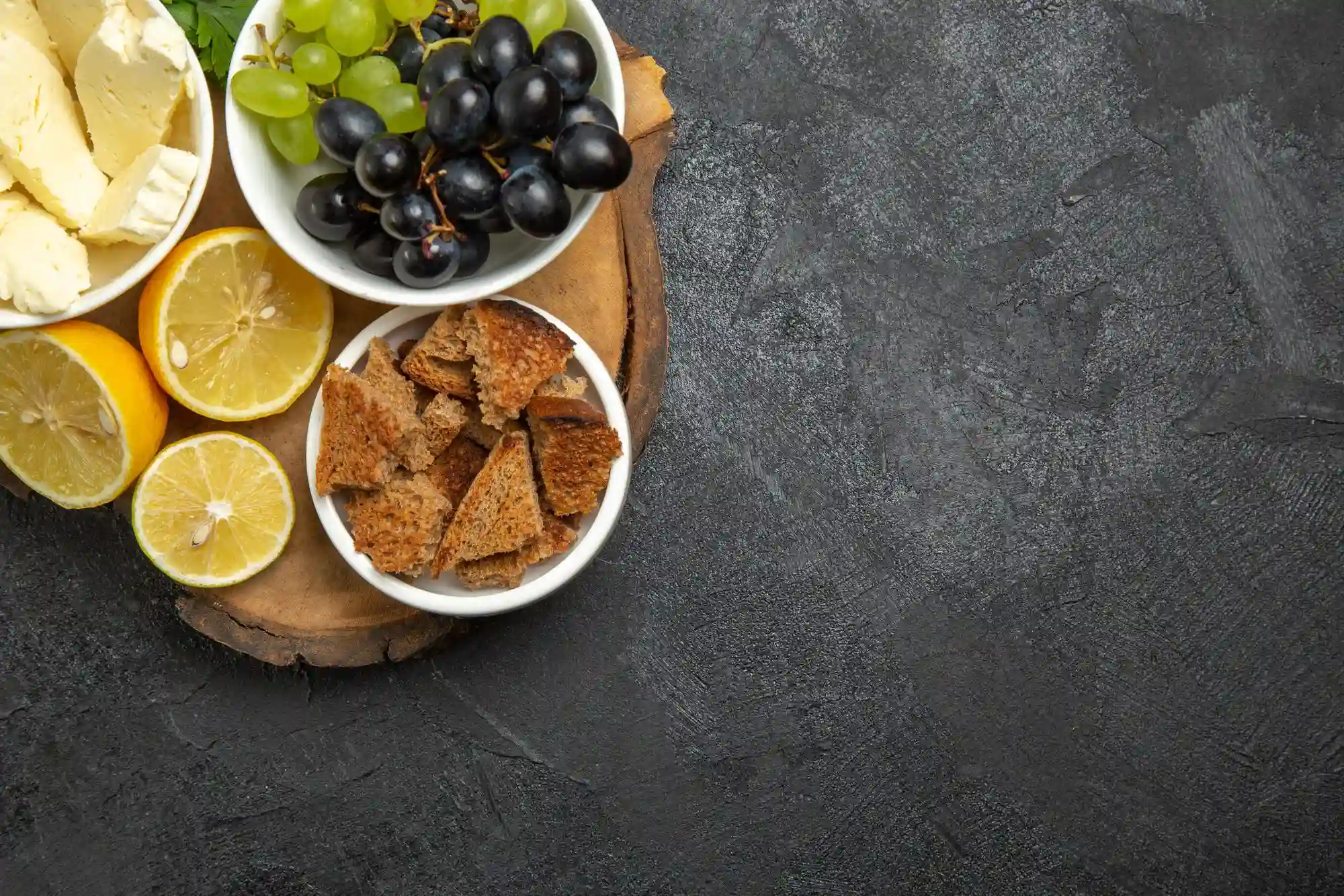 Cheese, lemons, and grapes on a dark background.