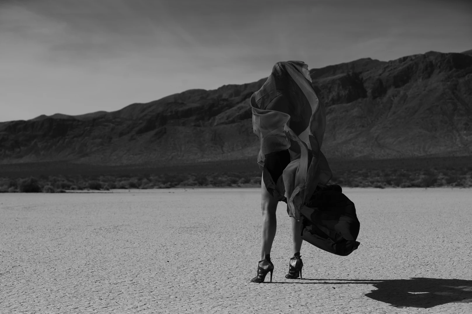 Black-and-white dynamic shot of the artist mid-motion, with fabric flowing in the desert wind.