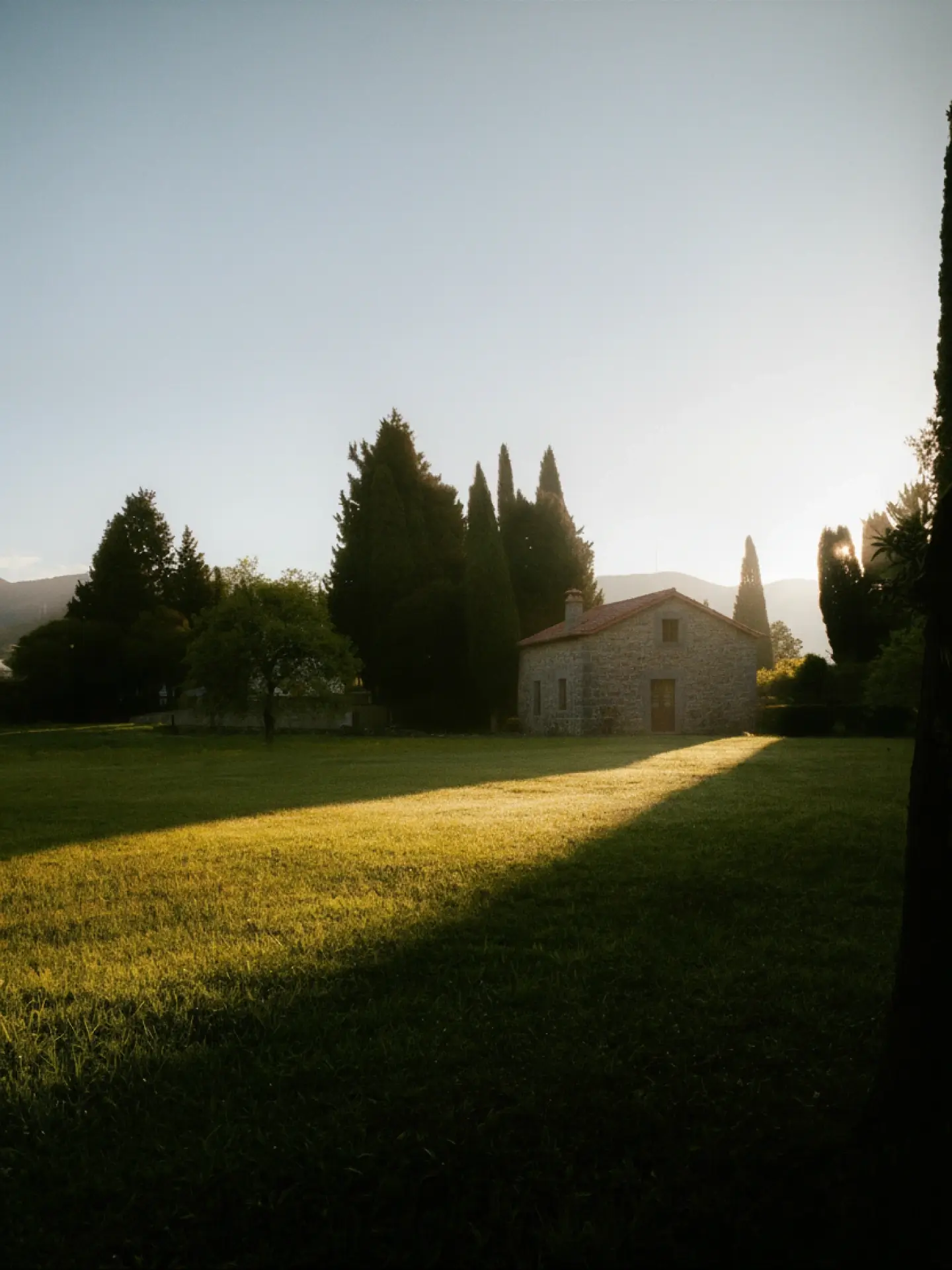 Stone farmhouse nestled among trees in soft morning light.