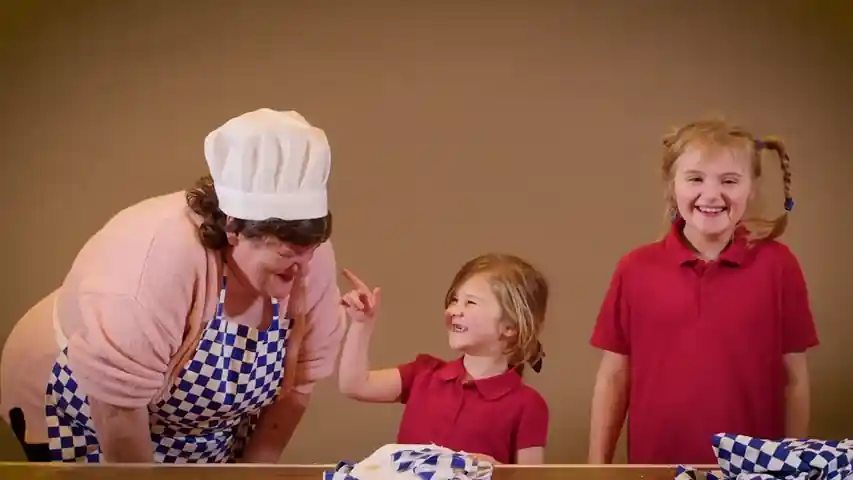 Adult and two children sharing a joyful moment while baking together in a community setting.