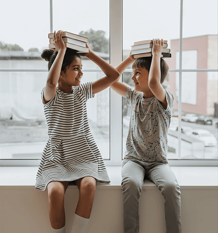 Two cheerful students are balancing books on their heads, smiling and laughing