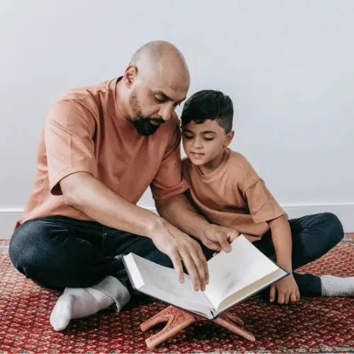 Father and young son sitting together reading a book on a wooden stand, serving diverse cultural communities across Melbourne's northern suburbs.
