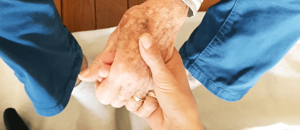 Les deux mains d'une professionnelle entourent la main d'une personne âgée