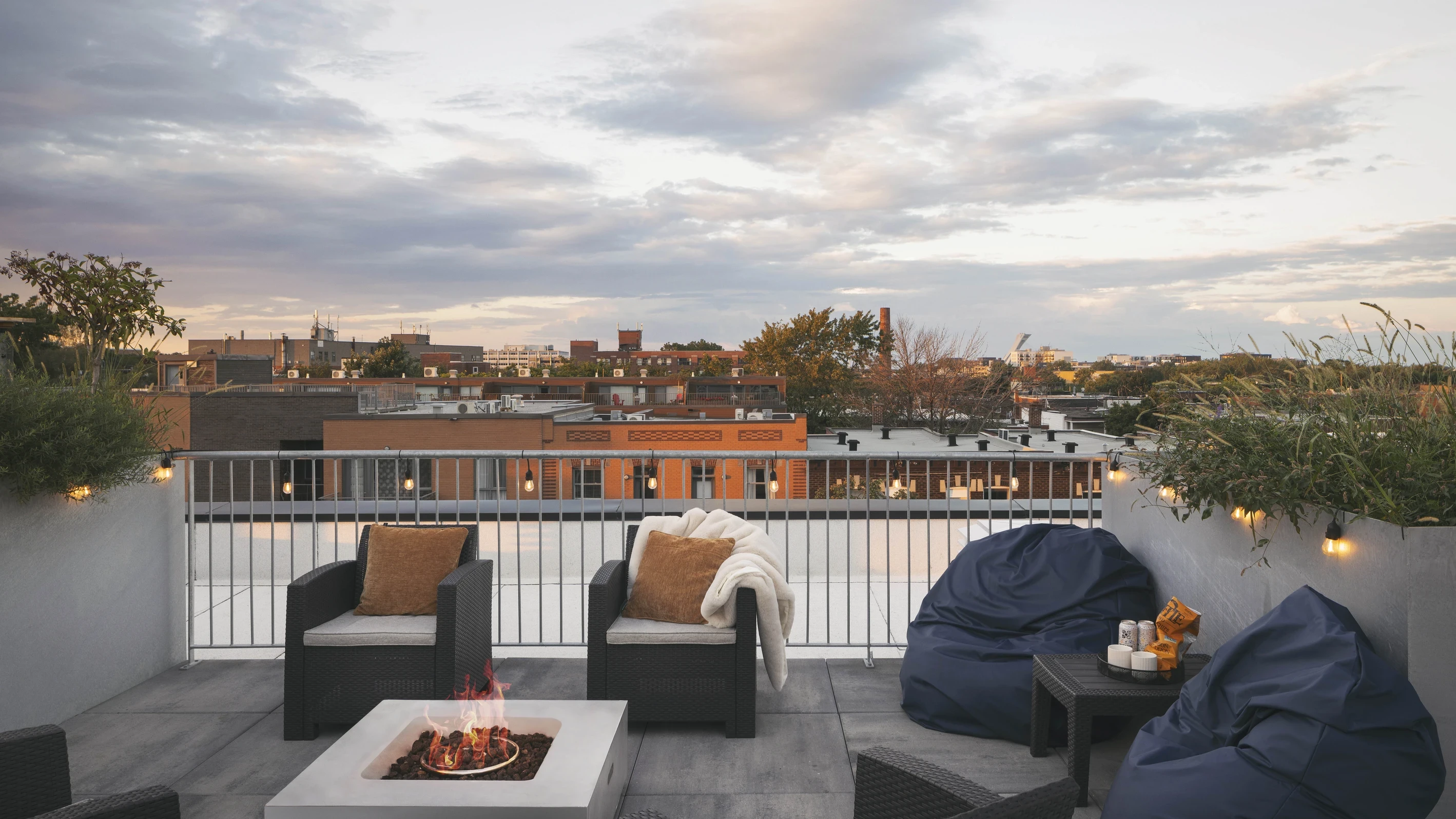 Terrasse résidentielle sur le toit à Montréal avec mobilier extérieur, foyer central et vue dégagée sur le quartier au coucher du soleil