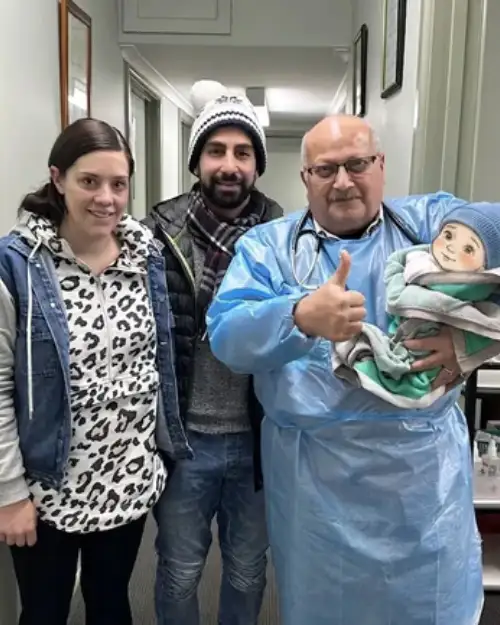 Dr. Ashraf Saddik holding a bundled infant wearing a beanie alongside a mother and father in the clinic hallway.
