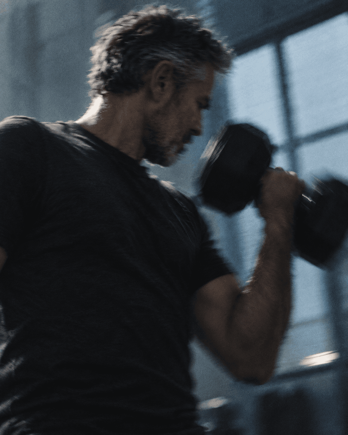 A middle-aged man strength training with a dumbbell in a gym
