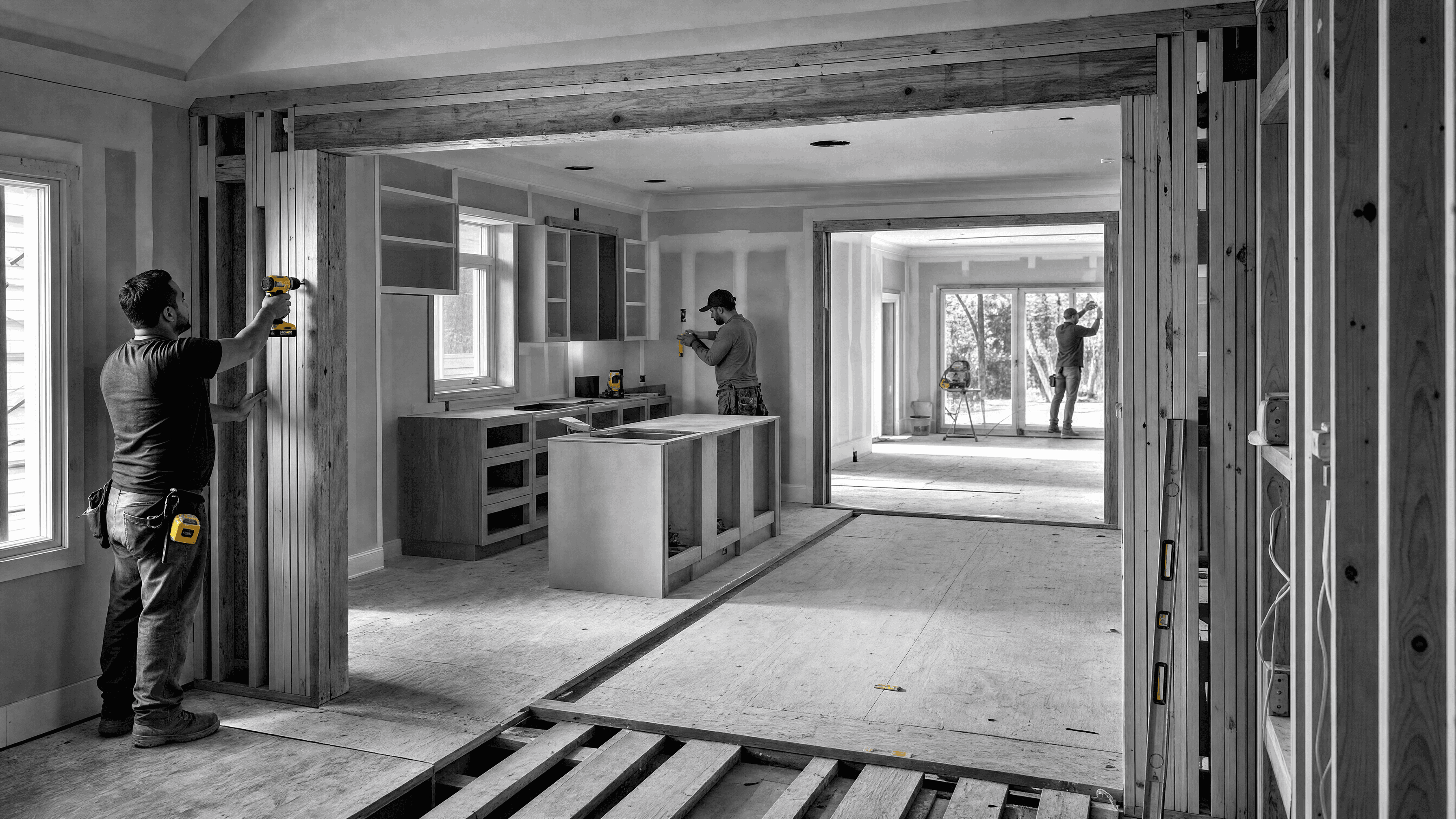 Three workers renovate connected interior zones with exposed framing, open floor structure, and partially installed cabinetry.