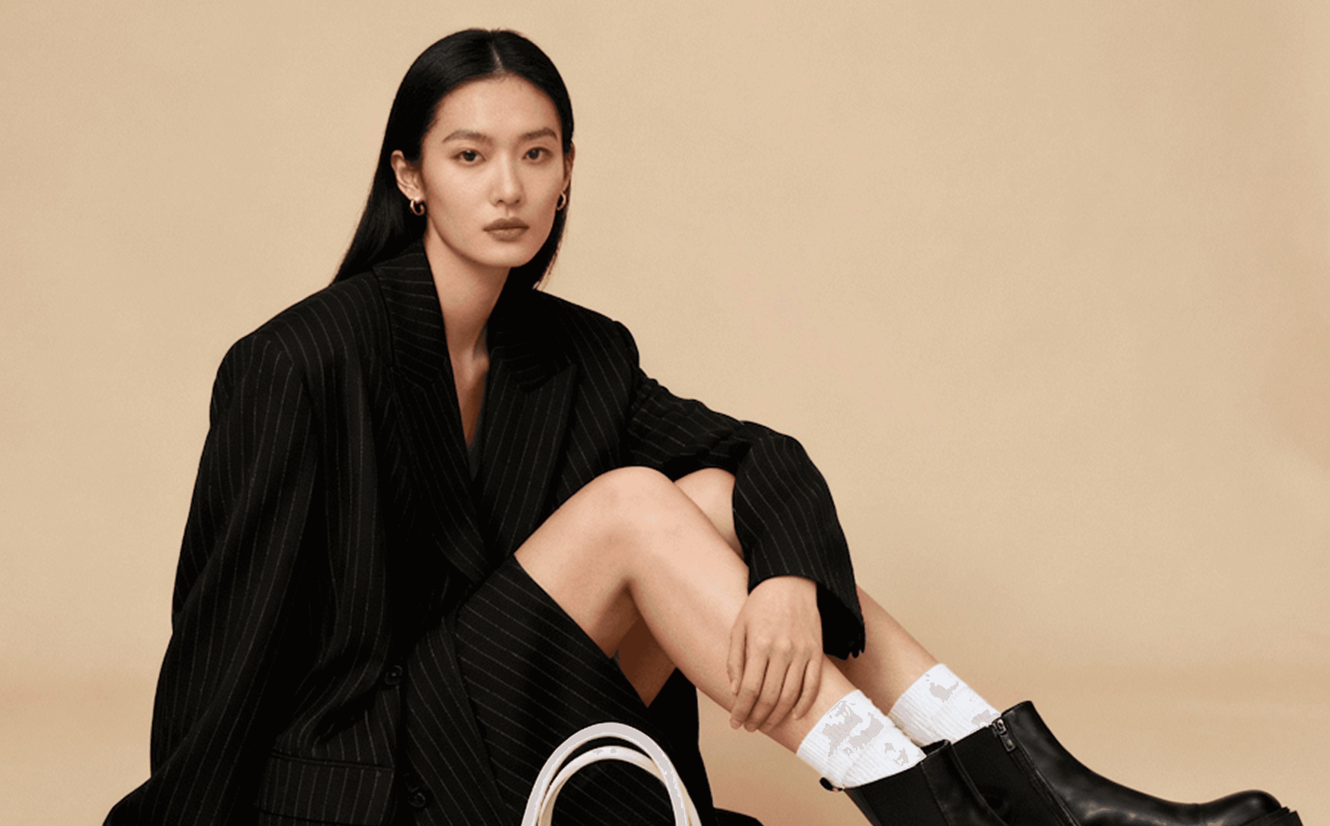 Woman in an oversized pinstripe blazer and skirt sitting on a beige floor.