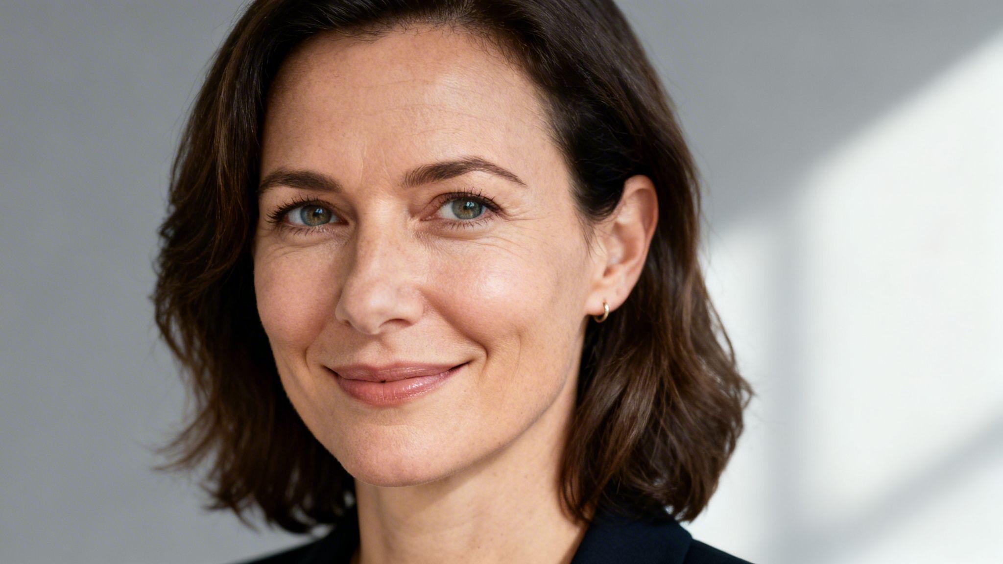 Nahaufnahme einer lächelnden Geschäftsfrau mit braunen Haaren und grünen Augen, die selbstbewusst in die Kamera blickt.