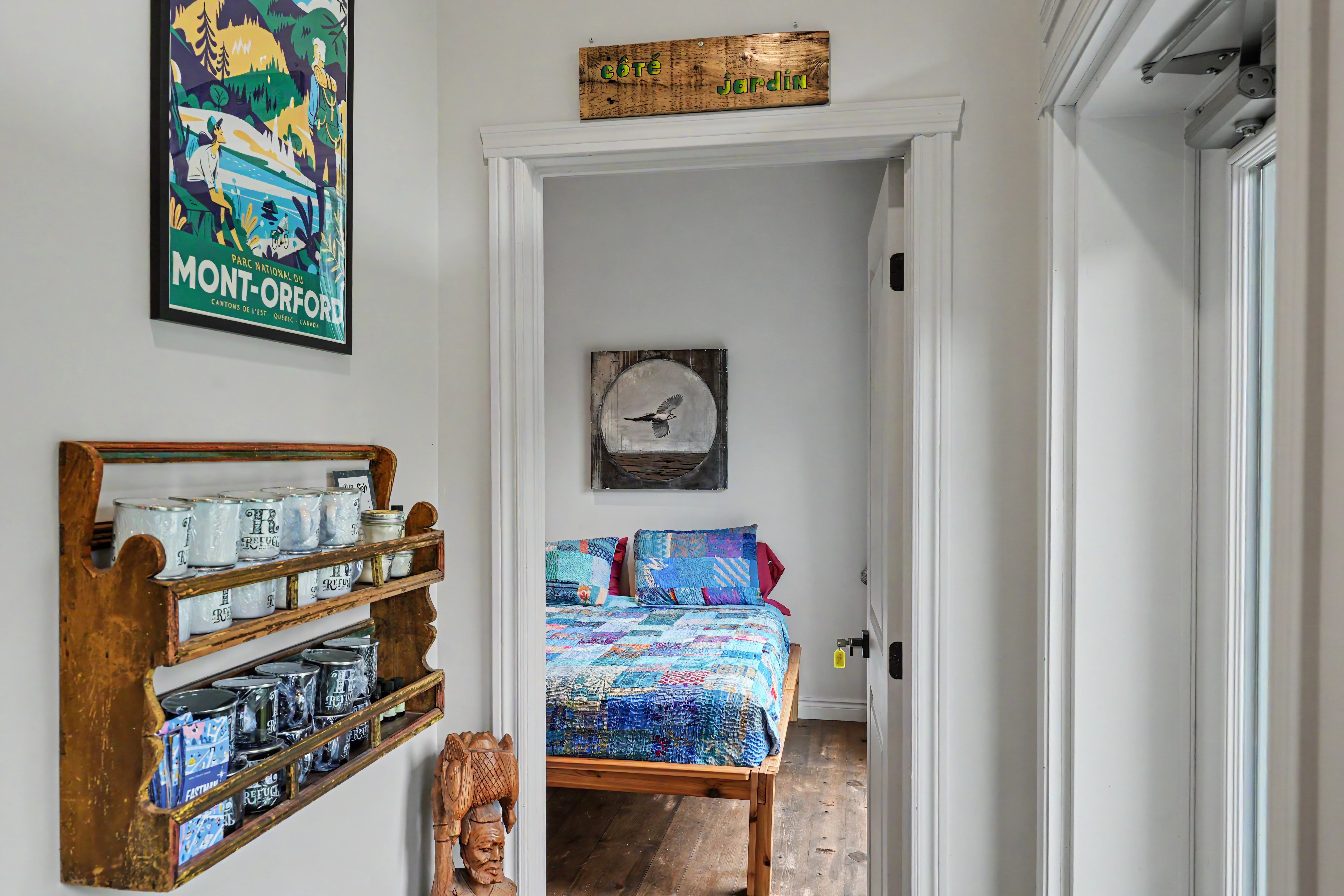 Chambre du gîte R112-Nord avec lit double recouvert d’une courtepointe patchwork bleue et verte, étagère murale en bois et affiche vintage du parc national du Mont-Orford.