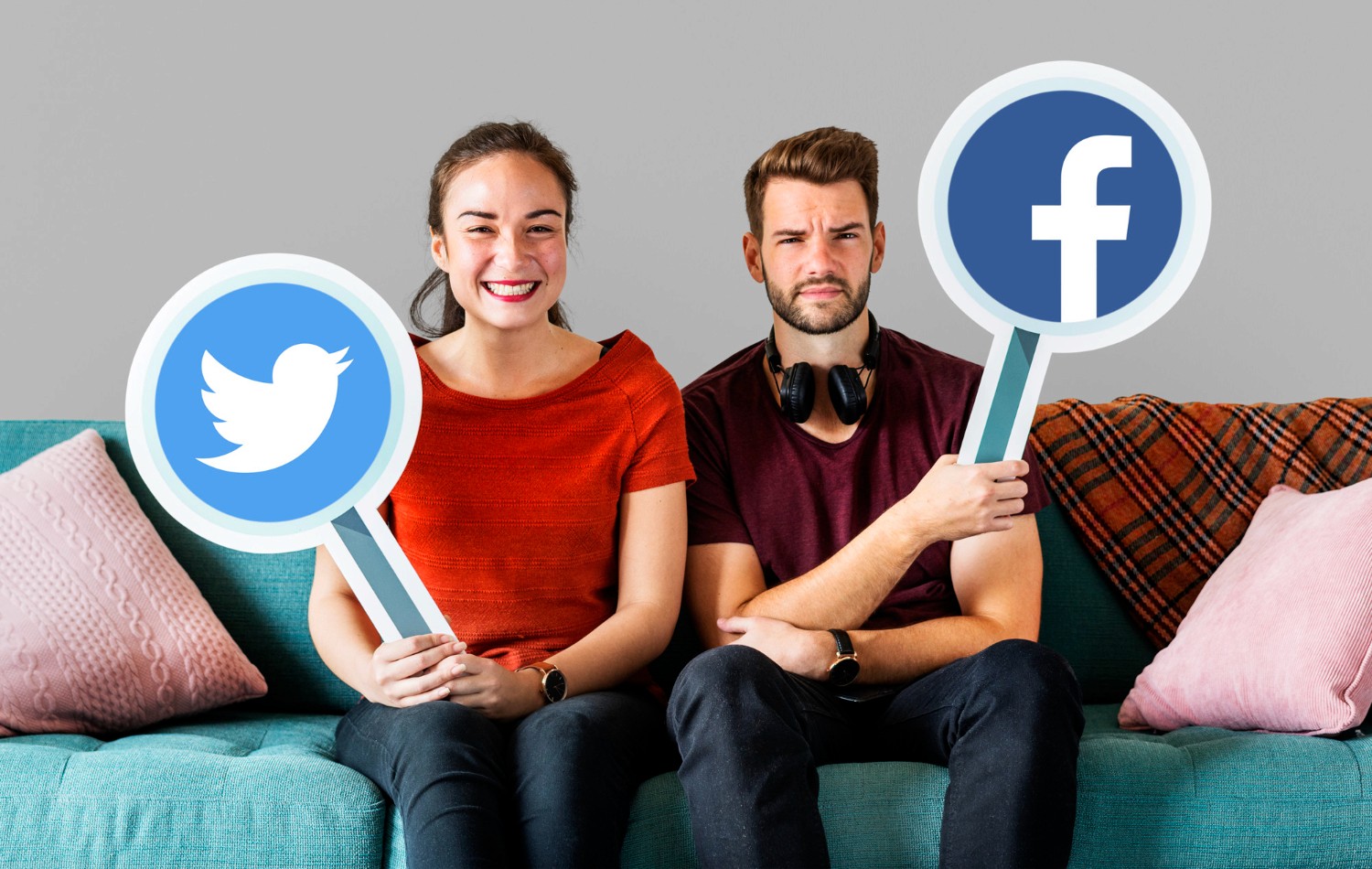  A man and woman on a couch, displaying signs featuring various social media icons, symbolizing digital communication.