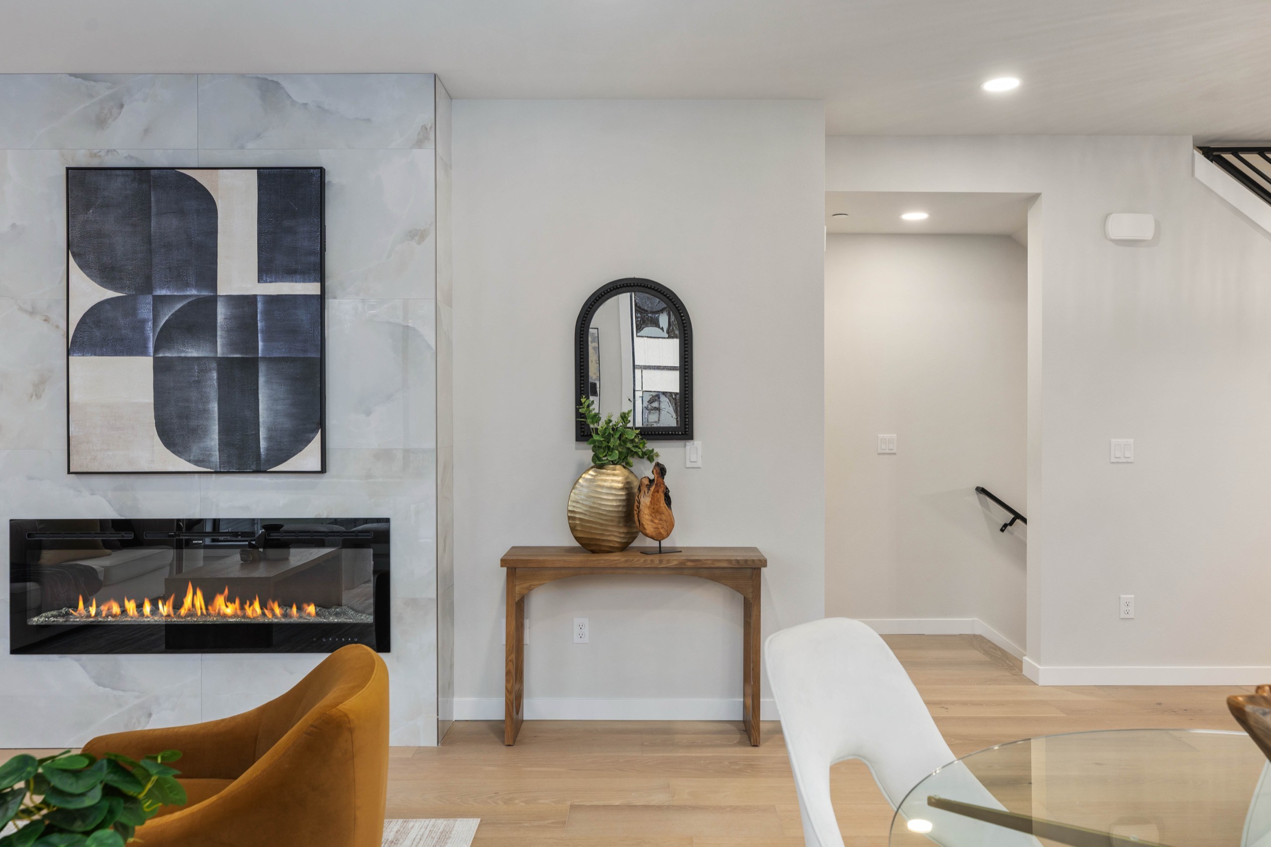 Luxury living room entry vignette with marble-surround linear gas fireplace, large abstract wall art, wooden console table, and light oak hardwood flooring