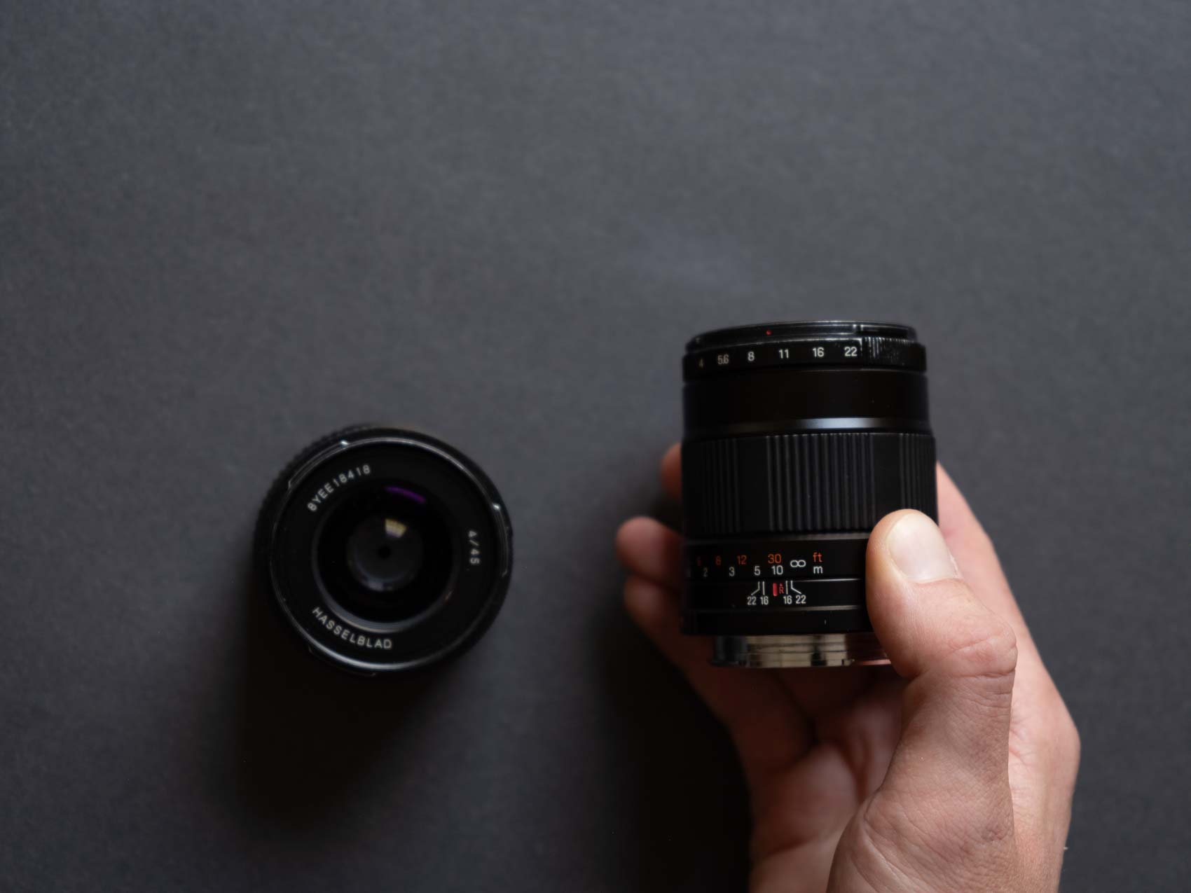 The Hasselblad XPan 90mm lens held in a hand next to the 45mm lens on the table