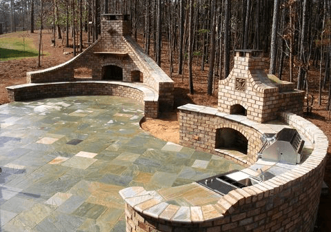 Curved stone patio with built-in fireplace, oven, and seating wall