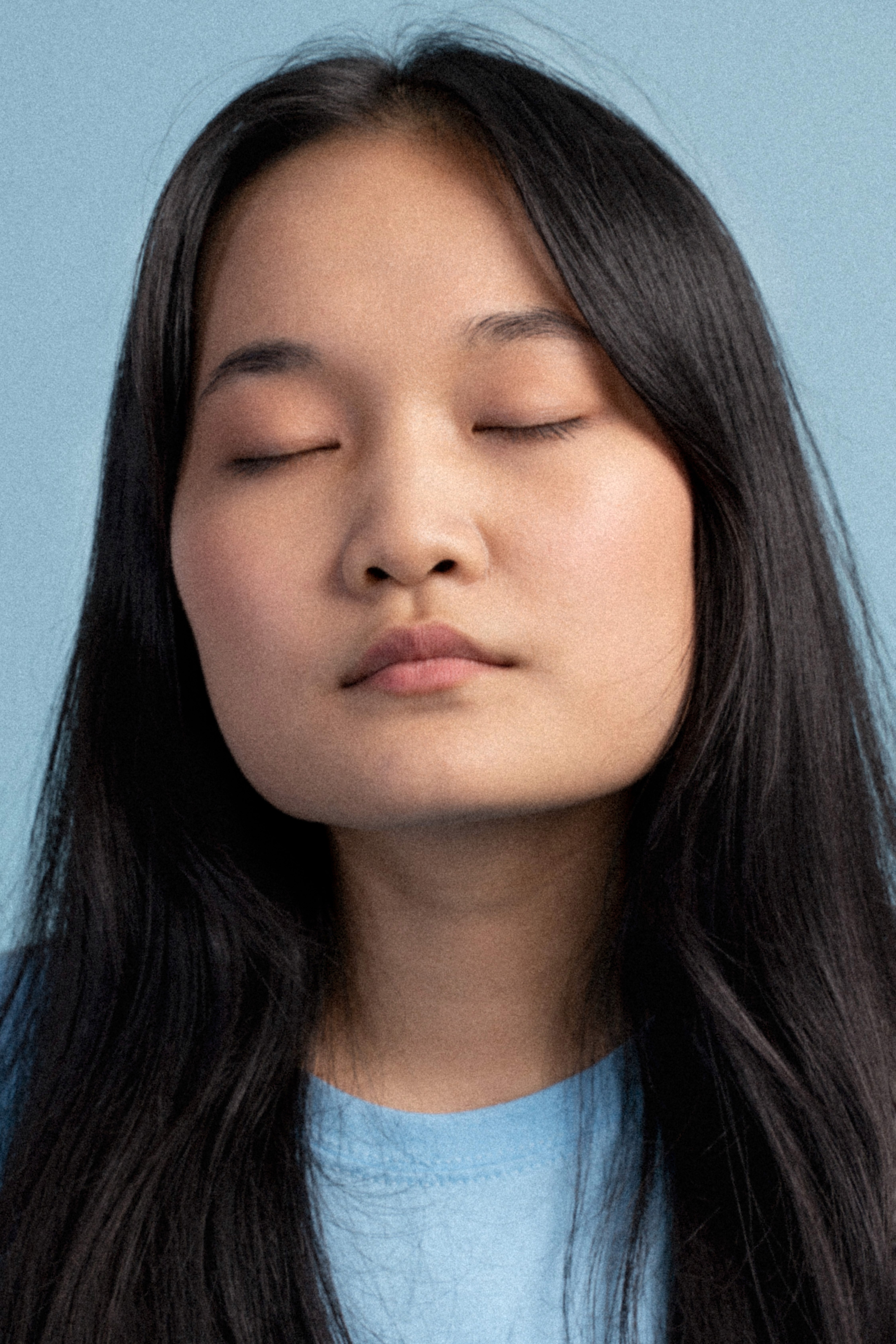 Calm young Asian woman with clear skin and no wrinkles, posed against a blue background.