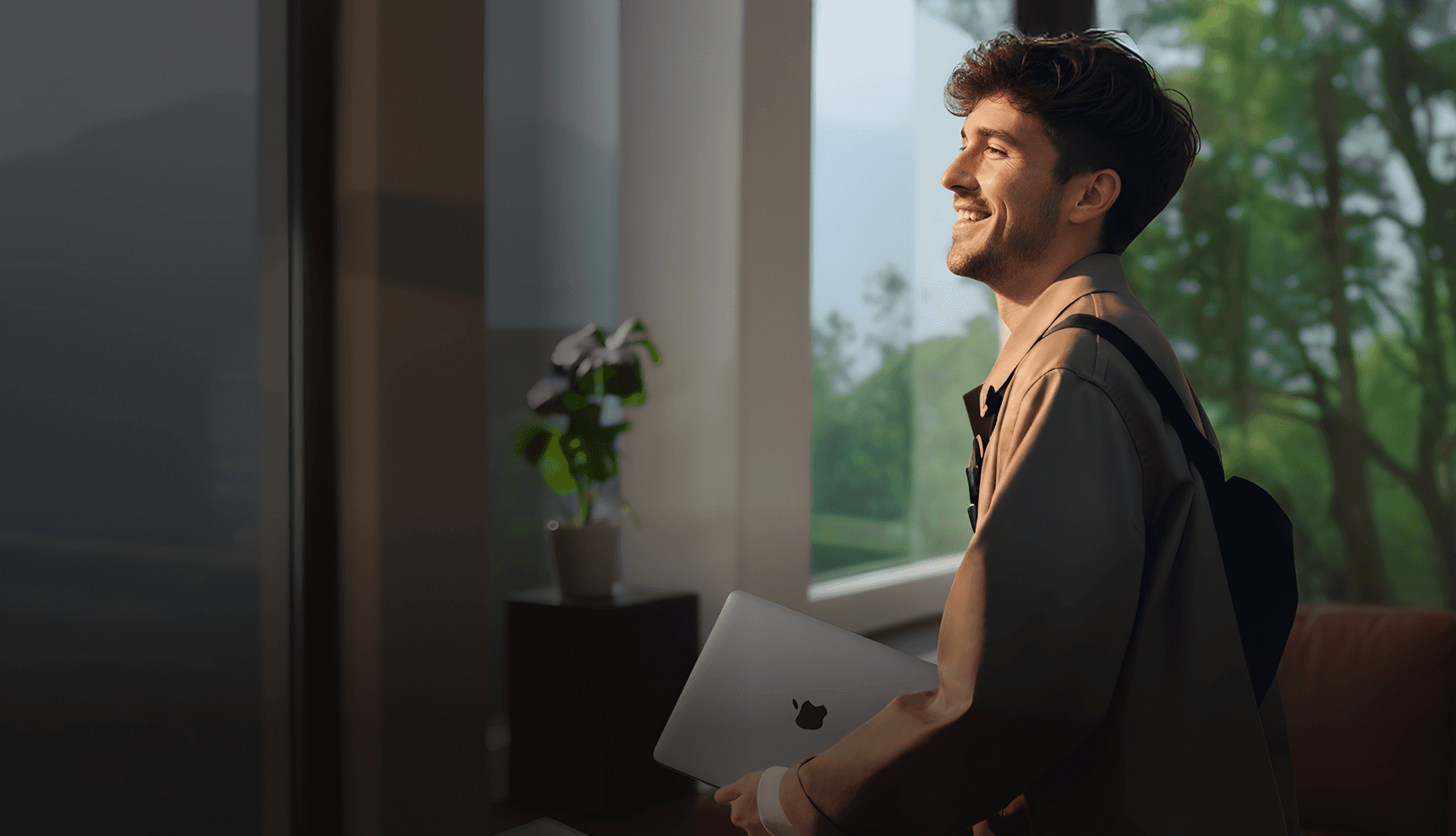 Become a channel partner - Happy man with a backpack holding a laptop looking out a window into the greenery.