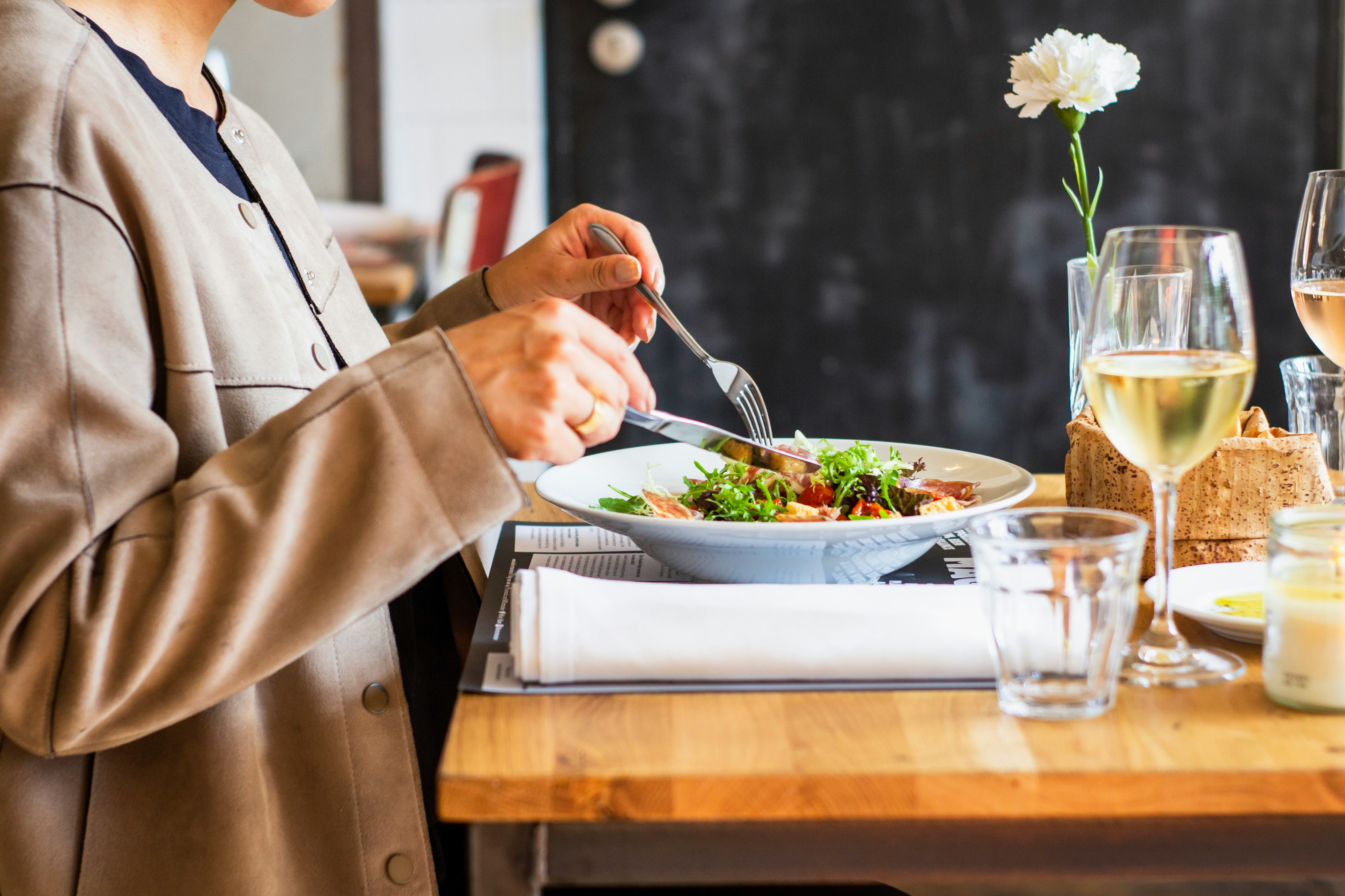 close-up of a woman sitting at a table eating a meal with a glass of wine