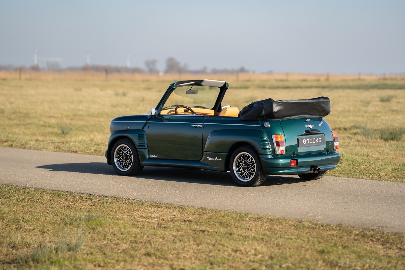 A convertible car parked on a dirt road, surrounded by open fields under a clear sky.