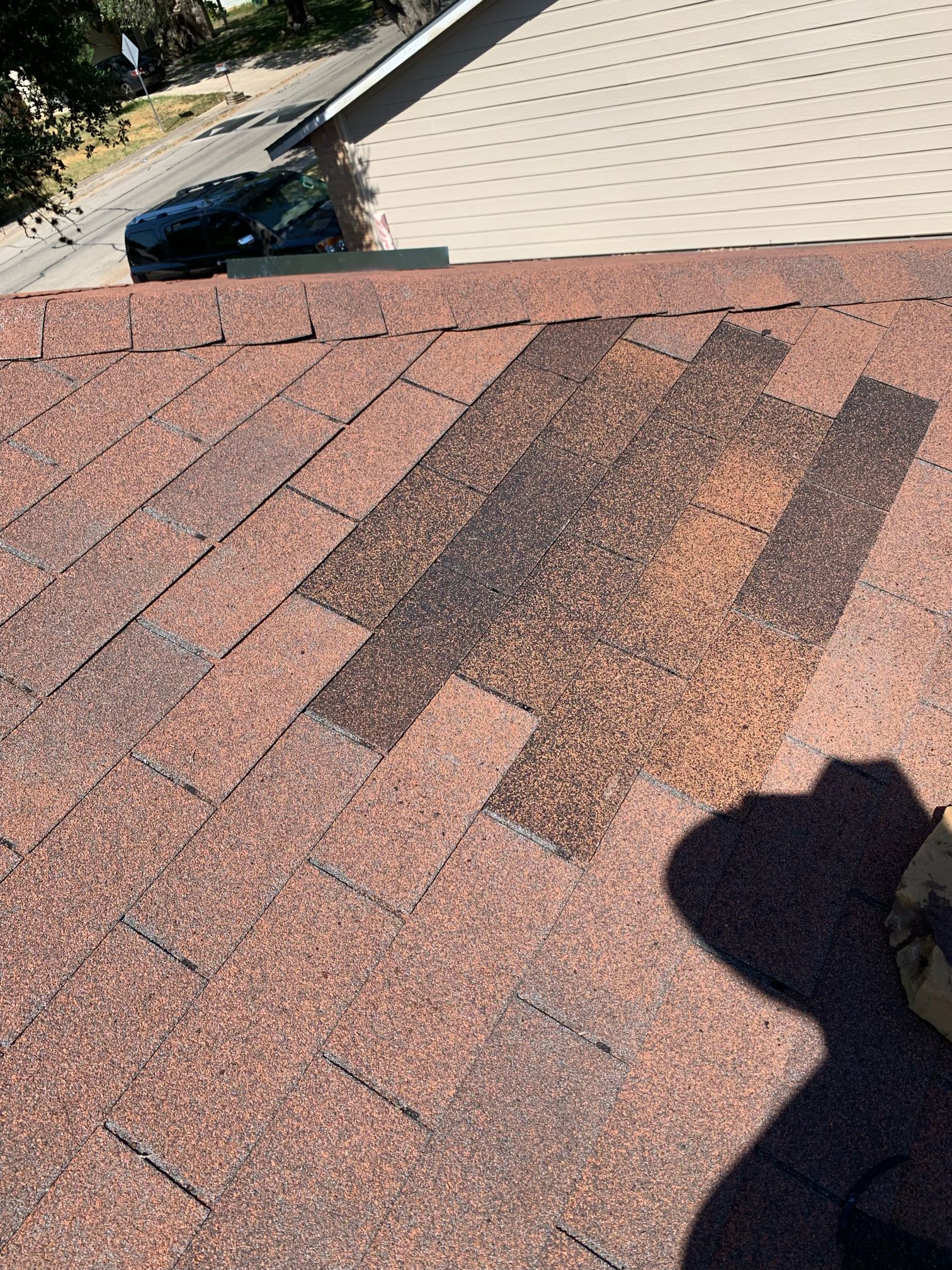 Shingle repair detail: a localized patch of darker architectural shingles beside the hip caps on the San Antonio roof.