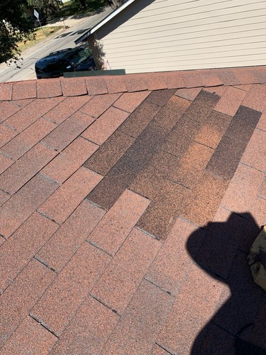 Shingle repair detail: a localized patch of darker architectural shingles beside the hip caps on the San Antonio roof.