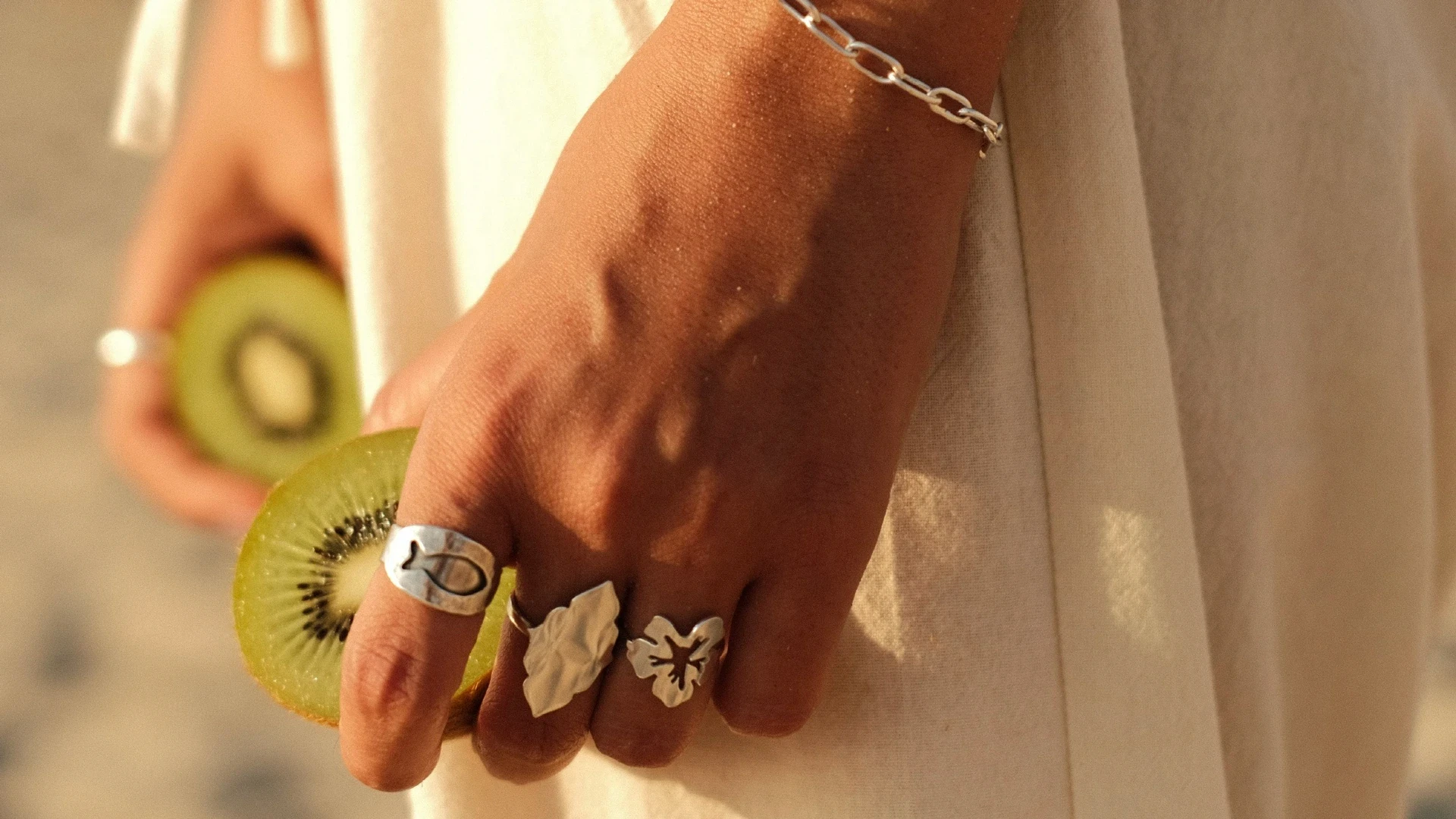 צילום לייף-סטייל אסתטי של יד אישה המעוטרת בטבעות כסף מעוצבות האוחזת בחצי פרי קיווי. התמונה משלבת טקסטורות טבעיות ותאורת שמש רכה, מאת Shiriz Photography והצלמת שירי עציץ.