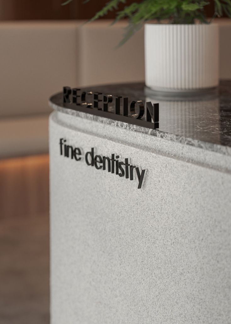 Reception desk signage with dimensional “RECEPTION” letters and “fine dentistry” logo on a textured stone counter in a modern dental clinic.