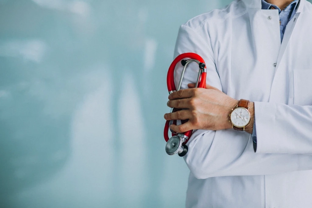 Cropped photo of a doctor's arm folded holding a red stethoscope.