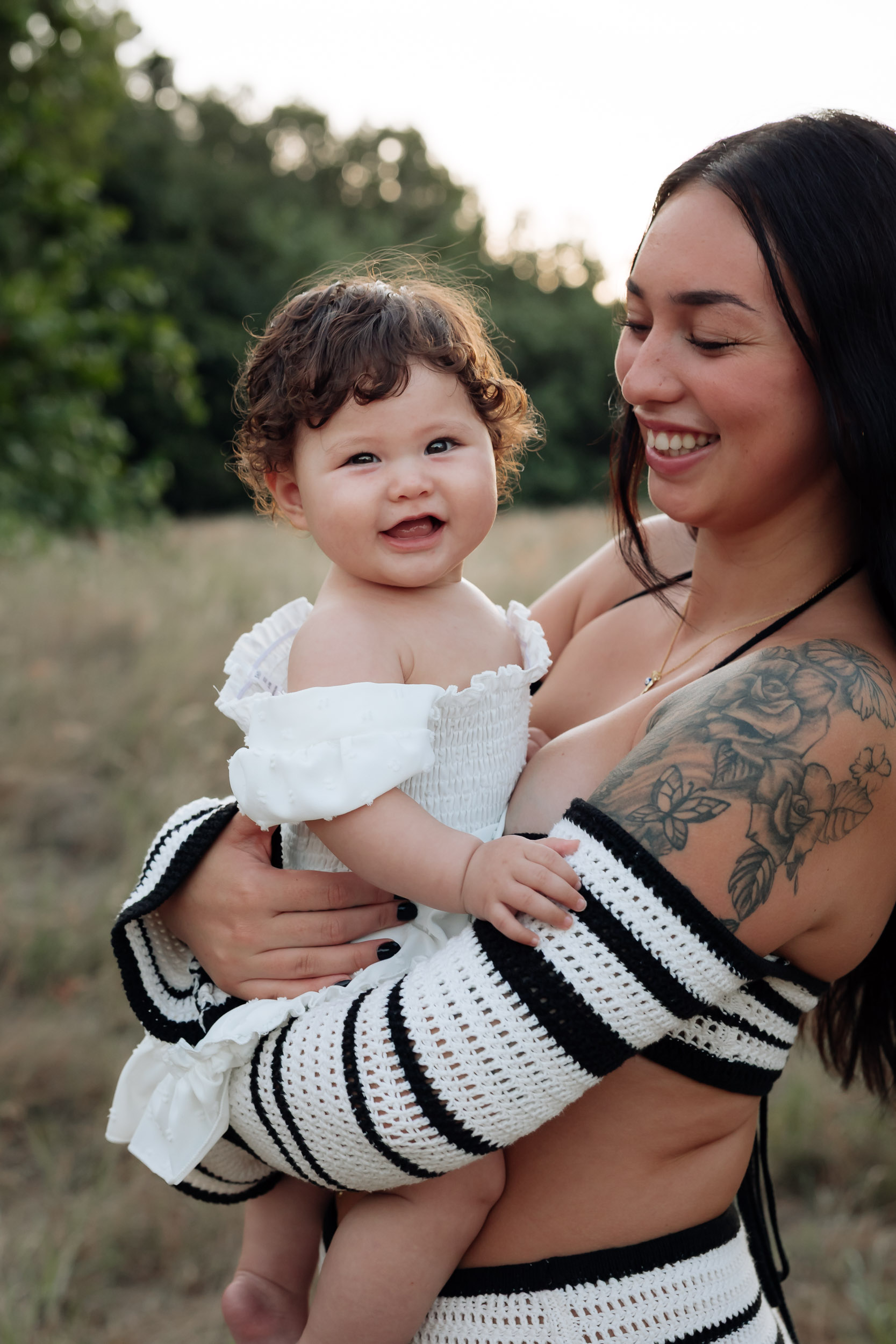 Mum holding her young daughter in a grassy field at sunset, capturing a quiet moment of connection during a natural motherhood photo session.