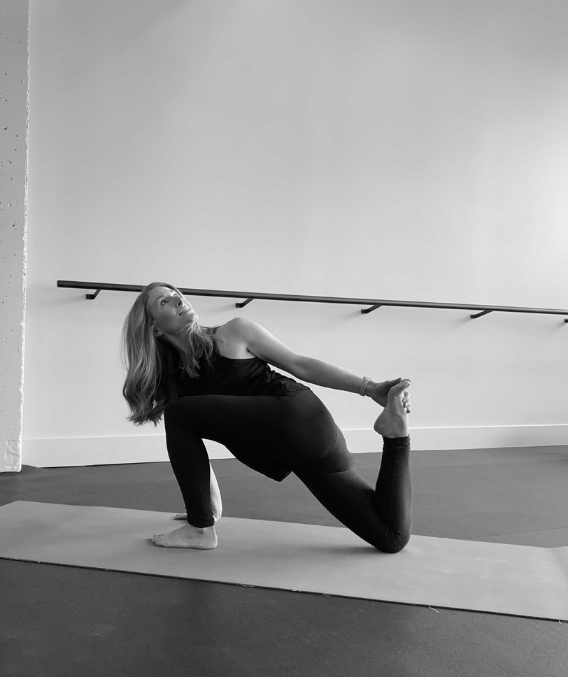 Heather Hausman performs a low lunge yoga pose on a mat in a minimalist studio, demonstrating flexibility and focus in a well-lit space.