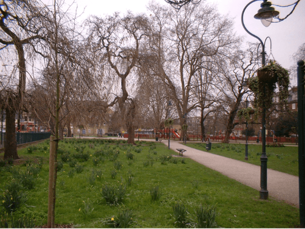 A smiling man with curly hair is sitting at a desk, looking at the camera, with a laptop and a lamp in the background.