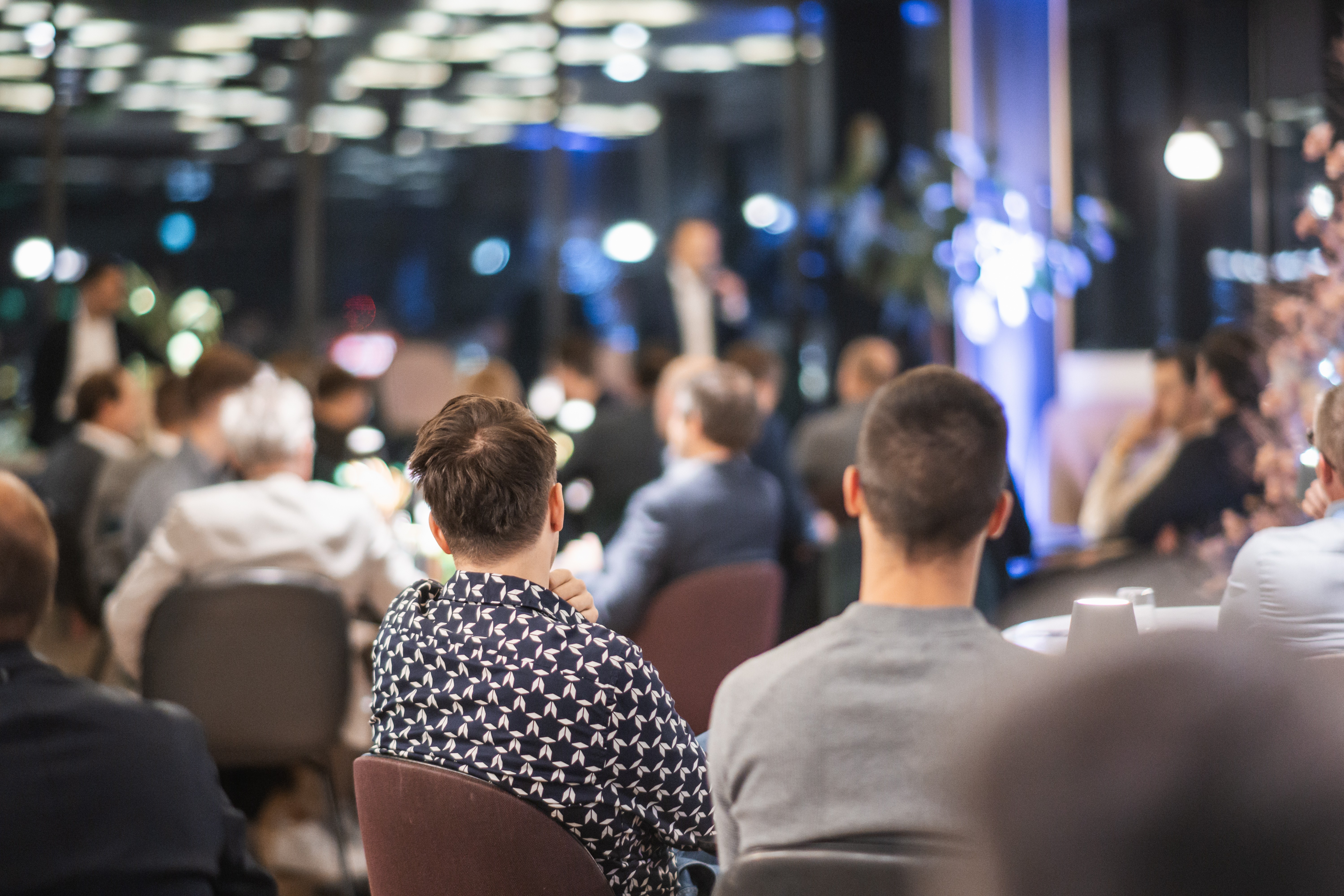 Attendees seated at a corporate committee meeting, listening to a presenter at the front of the room.