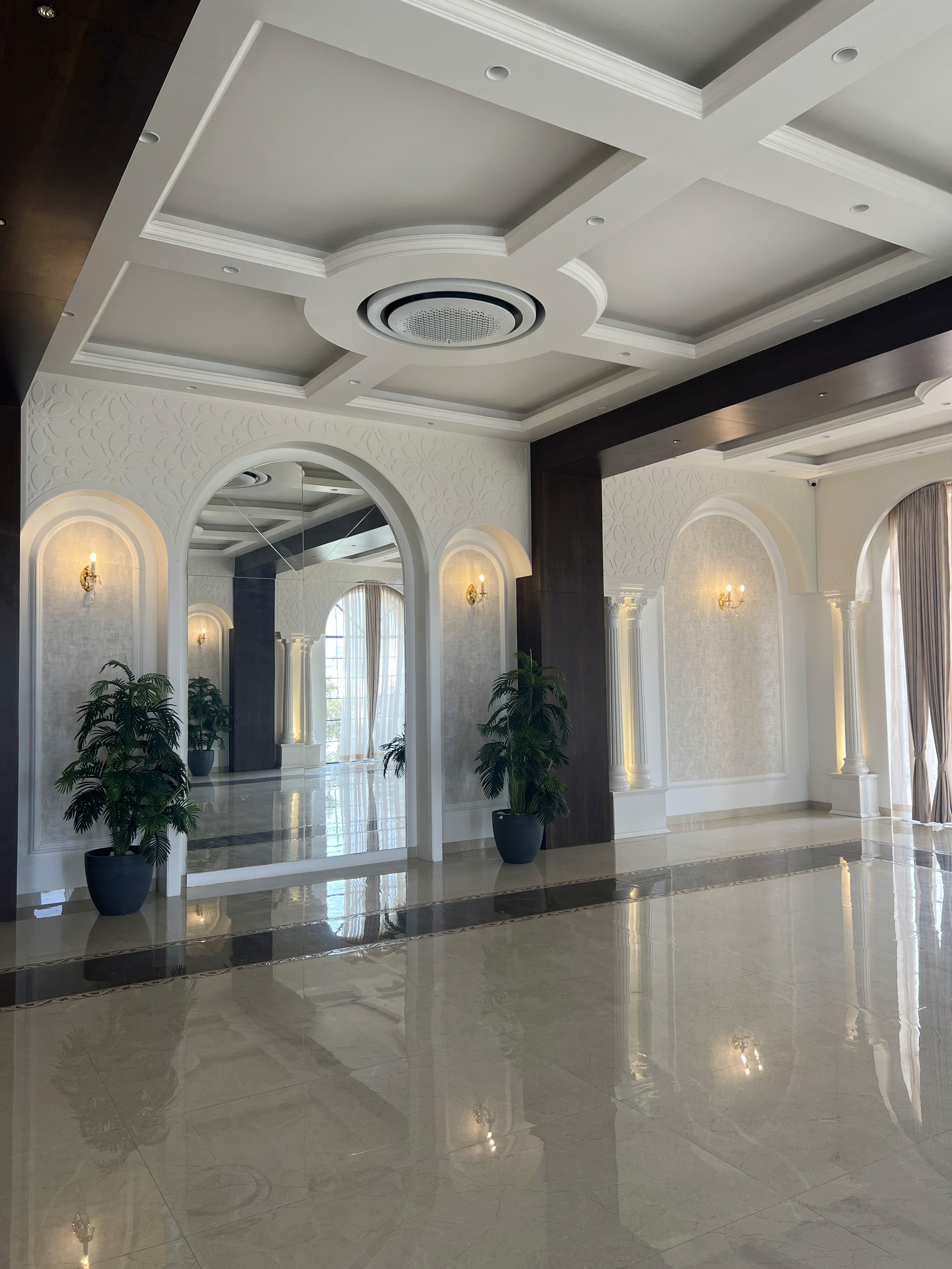 Luxurious commercial hall interior featuring highly polished marble floors, an elegant coffered white ceiling with recessed lighting, and large arched doorways.