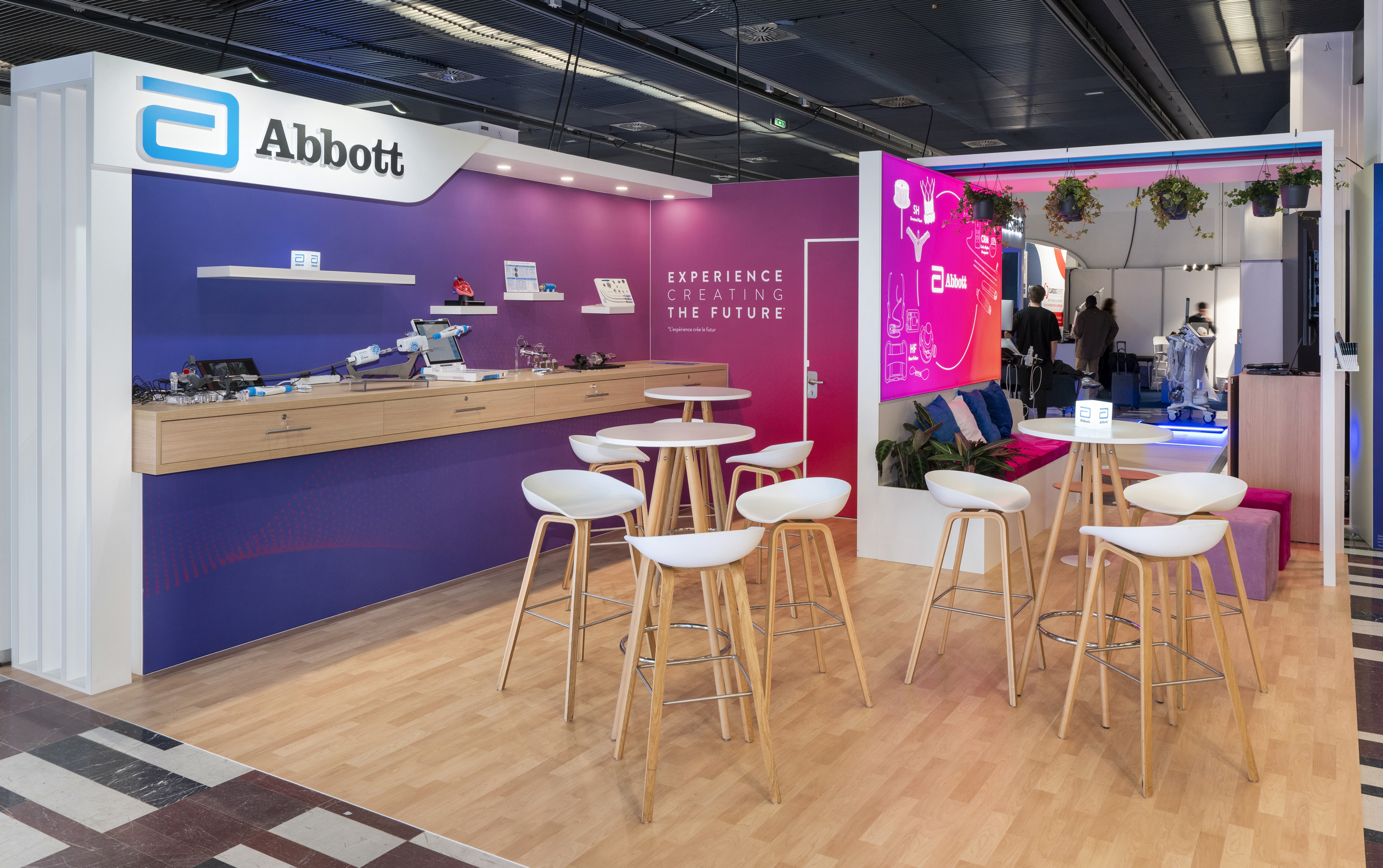 Stand Abbott JESFC 2026 conçu par Expace – vue d'ensemble avec dégradé bleu marine et rose magenta, écran grand format gammes cardiaques, zone banquette lounge et totem programme congrès