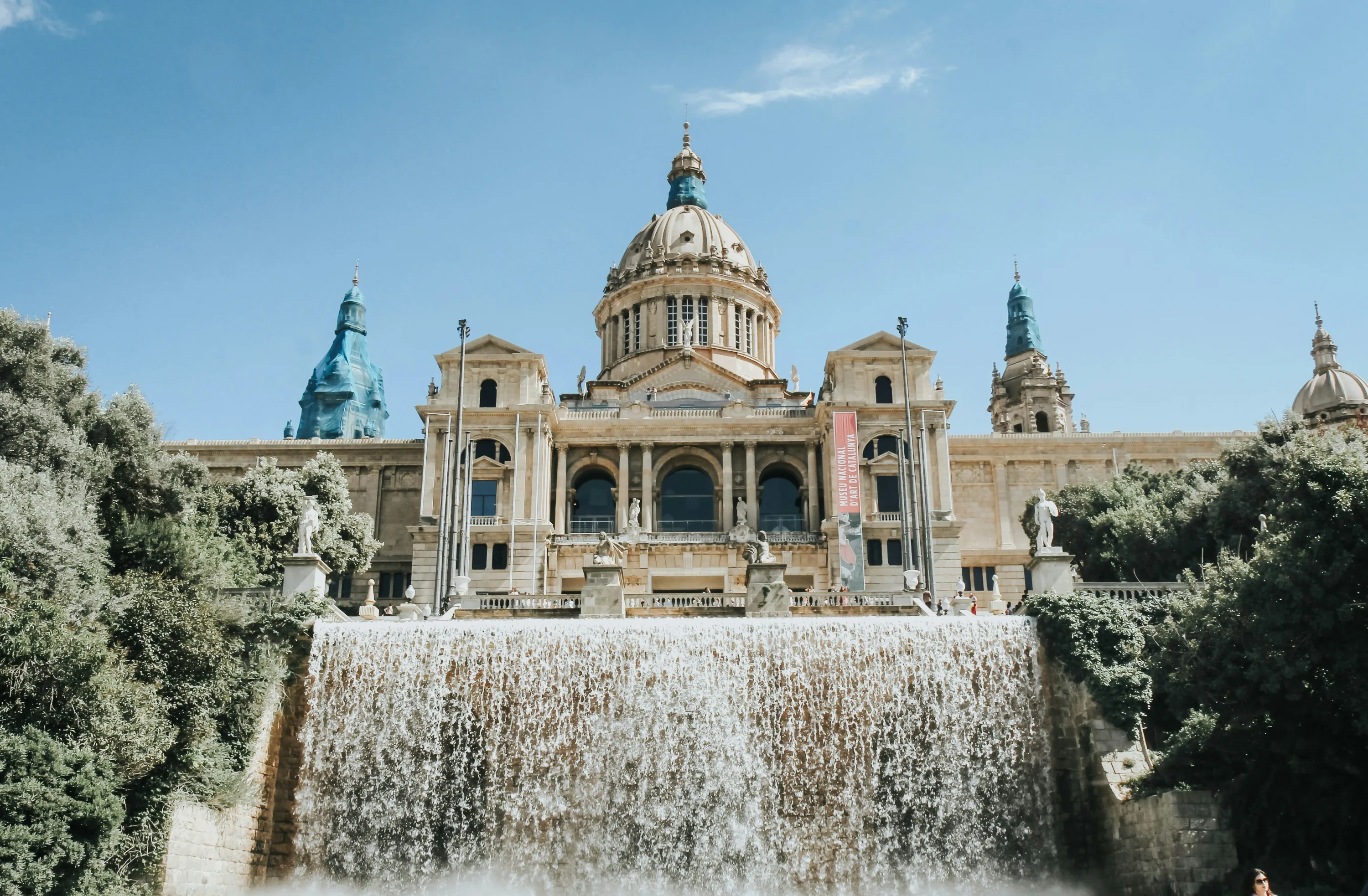 The dome of the Museu Nacional d'Art de Catalunya main building, with a waterfull from a large fountain pouring water at the forefront. 