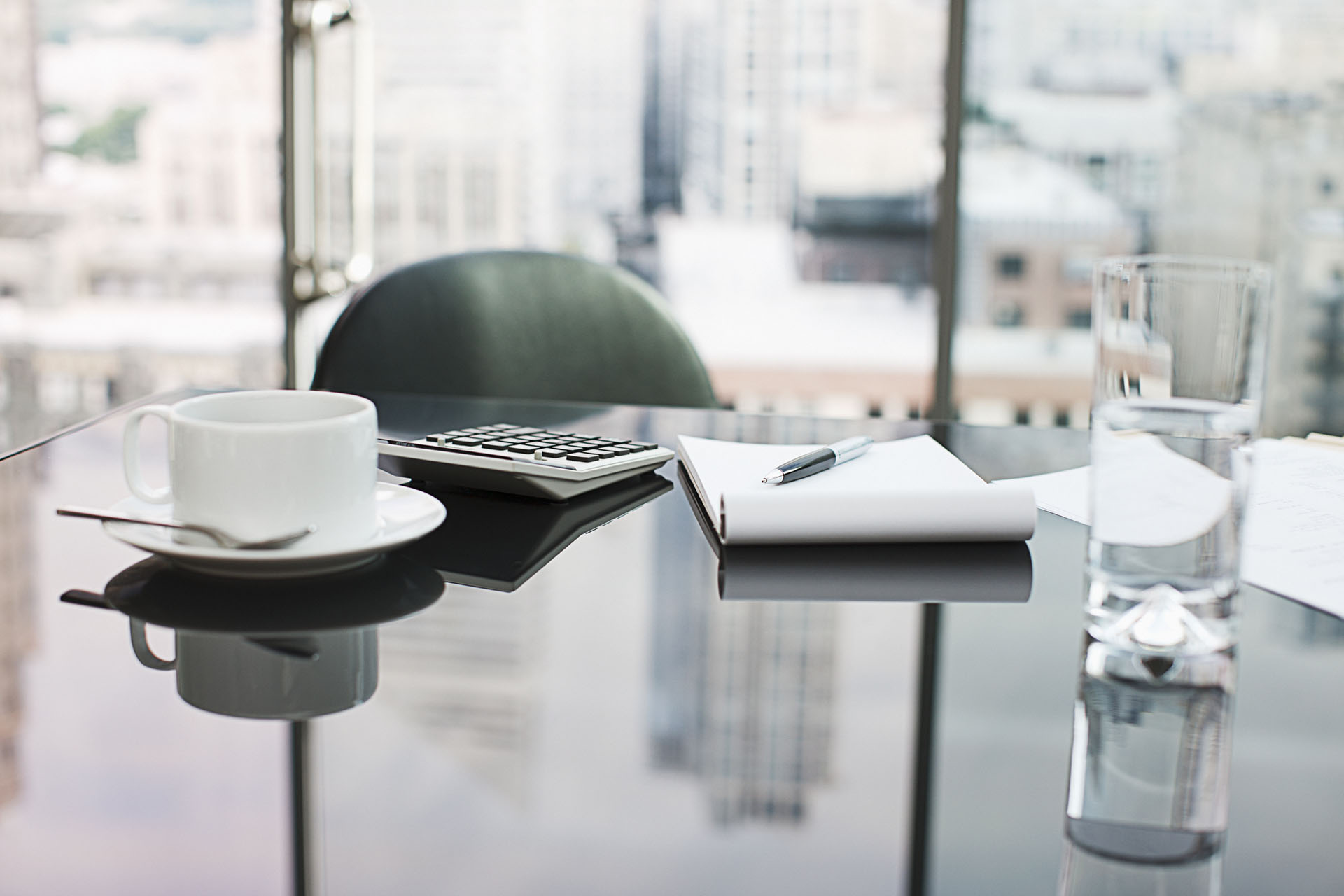 Blick auf einen Glastisch in einem schicken Büro, im Hintergrund ist unscharf eine Großstadt zu erahnen
