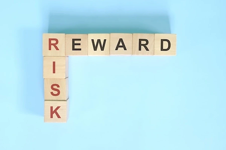 Wooden letter blocks spelling “RISK” vertically and “REWARD” horizontally on a light blue background.