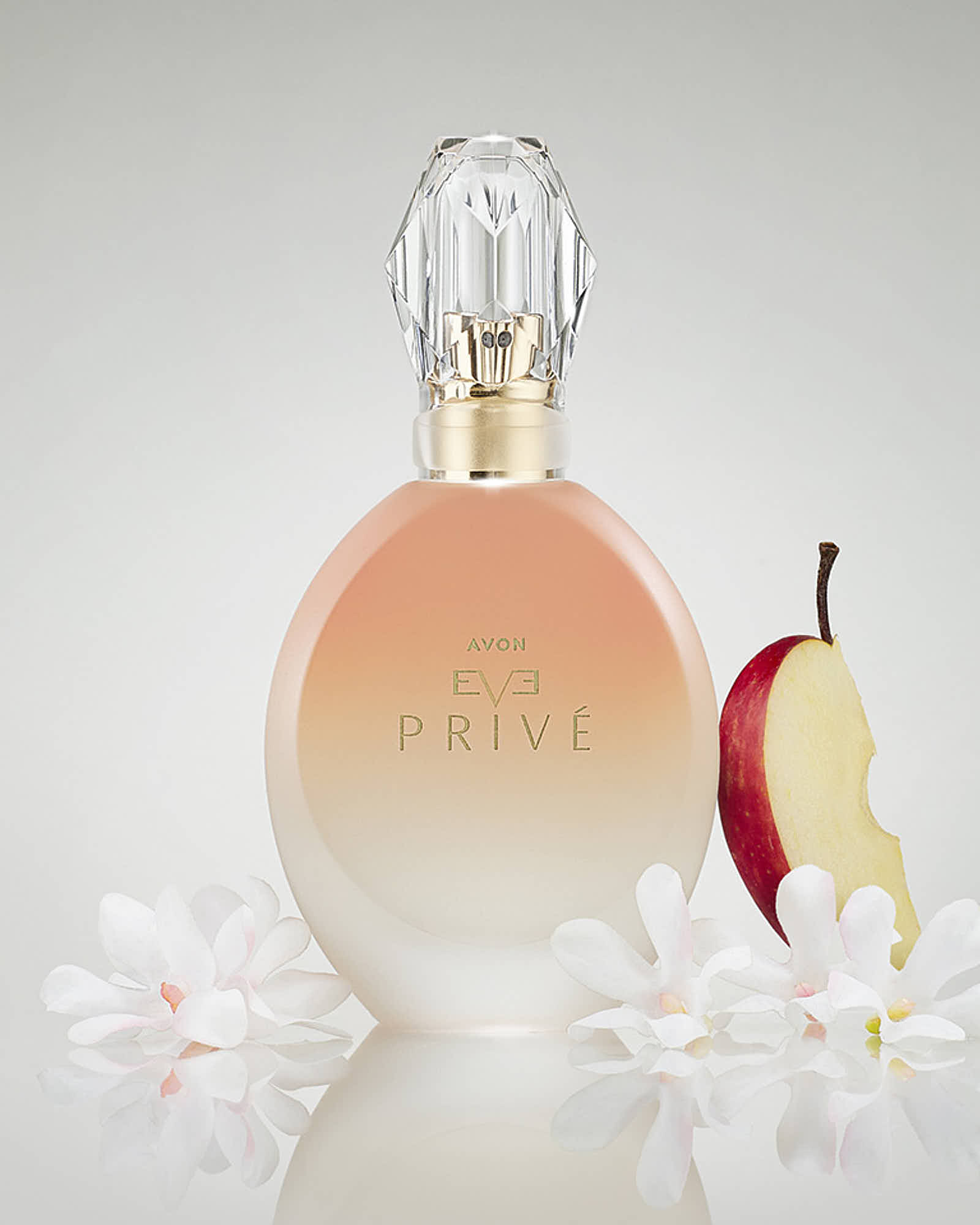 A bottle of perfume with an elegant design, next to a sliced apple and surrounded by white flowers.