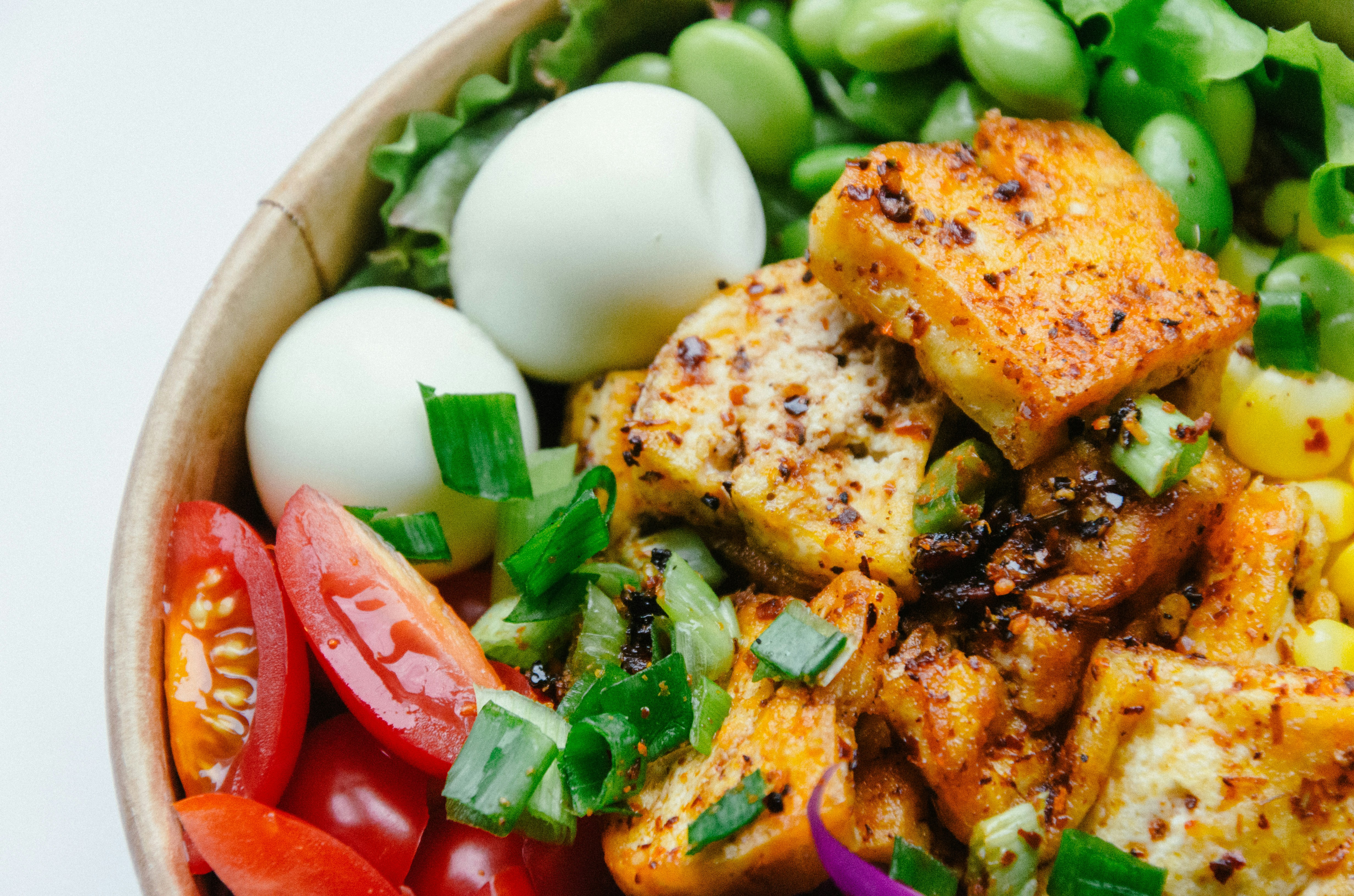 A bowl of seasoned tofu with boiled eggs, tomatoes, edamame and greens, low-FODMAP proteins and vegetables many people tolerate well with SIBO