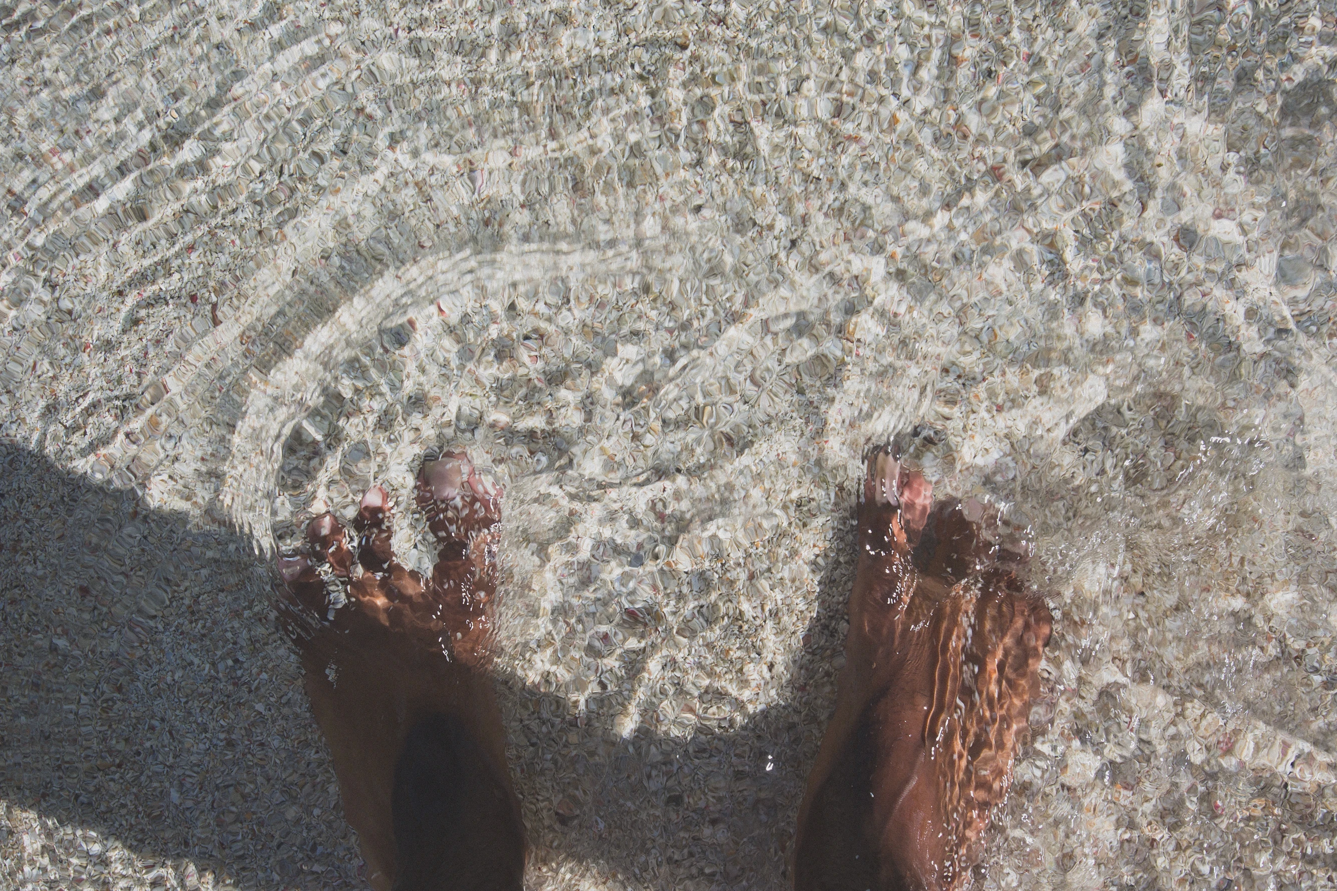 A pair of feet in shallow water on a beach.