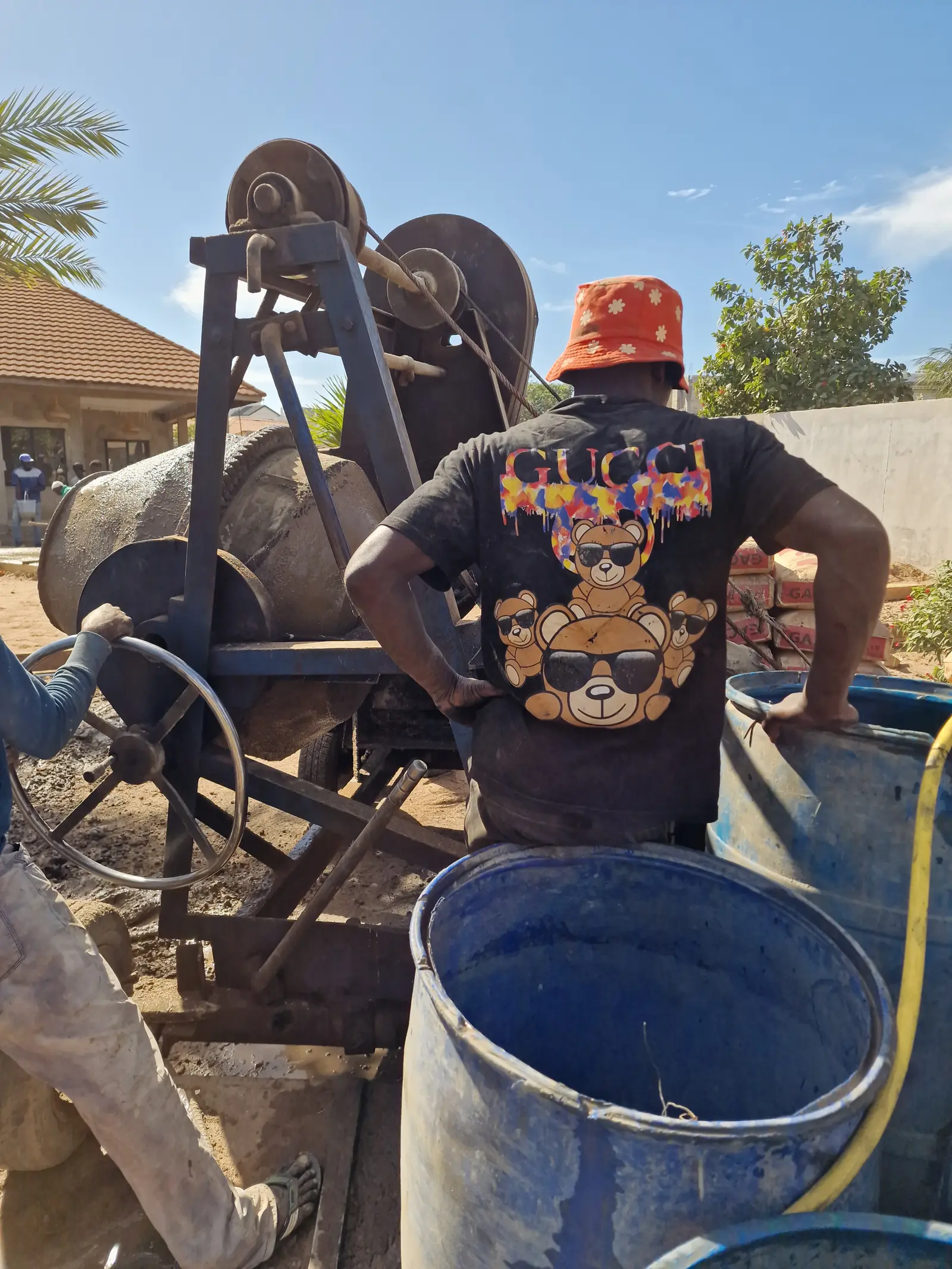 A person in a black shirt with colorful graphics operates machinery outdoors under a clear blue sky.