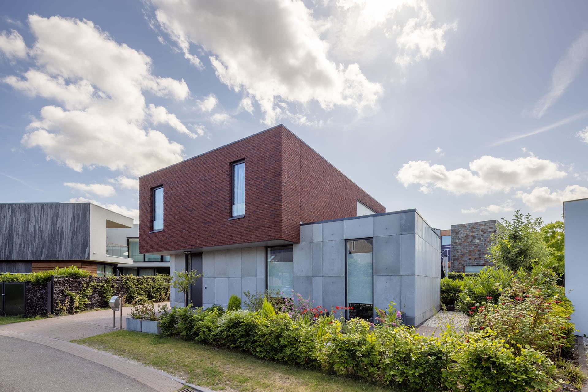 Straatzijde van Villa Rijswijk met rood metselwerk, betonlook plint en voortuin.
