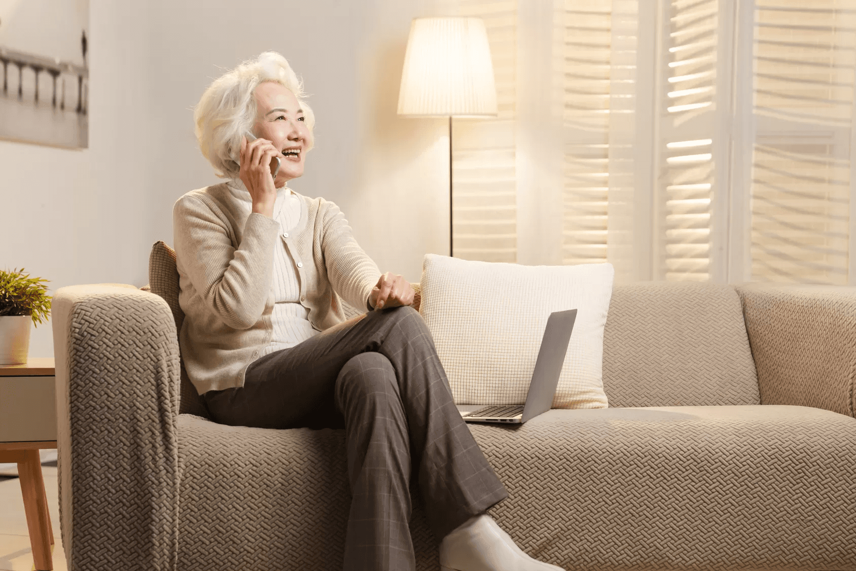 Image of a woman sat on a couch, talking on the phone and smiling