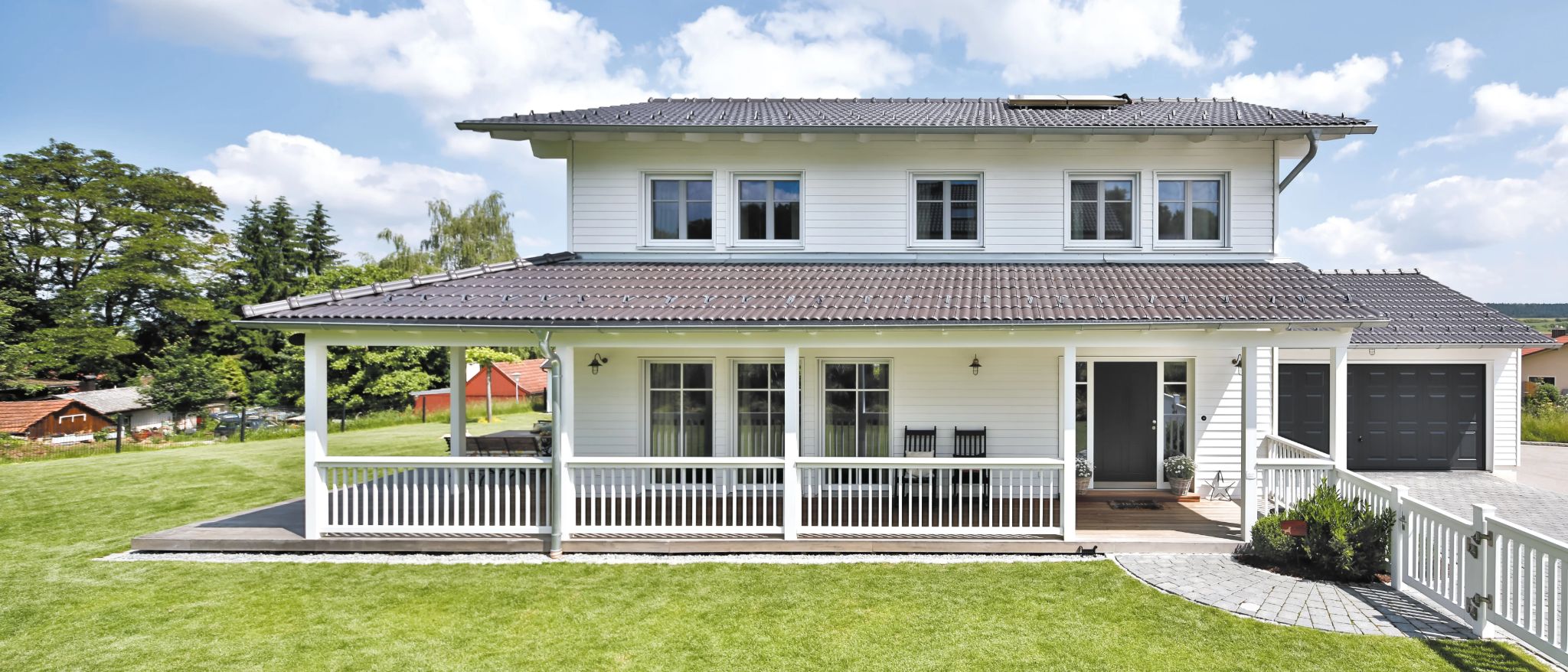 Modernes weißes zweistöckiges Haus mit Walmdach, Veranda, Garage und gepflegtem Garten.