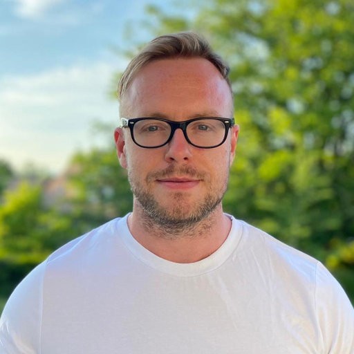 Matthew Vowels in a white tshirt with a green background and blue sky